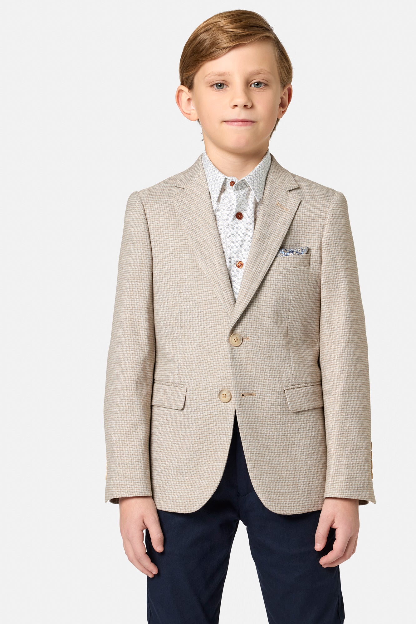 Young boy wearing a beige blazer over a white shirt with a patterned pocket square on a white background