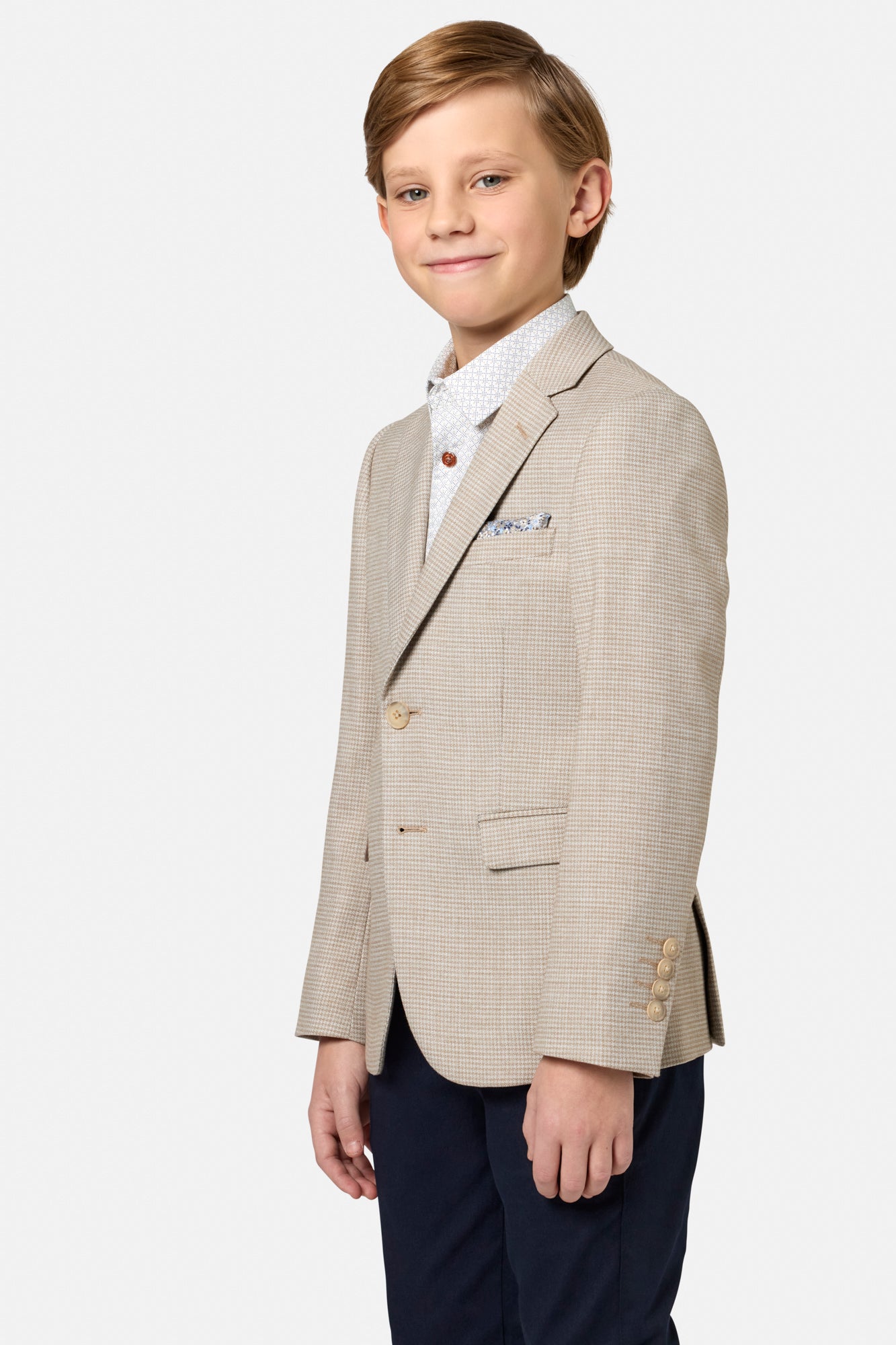 Young boy wearing a beige checkered blazer with a white shirt and navy pants on a white background