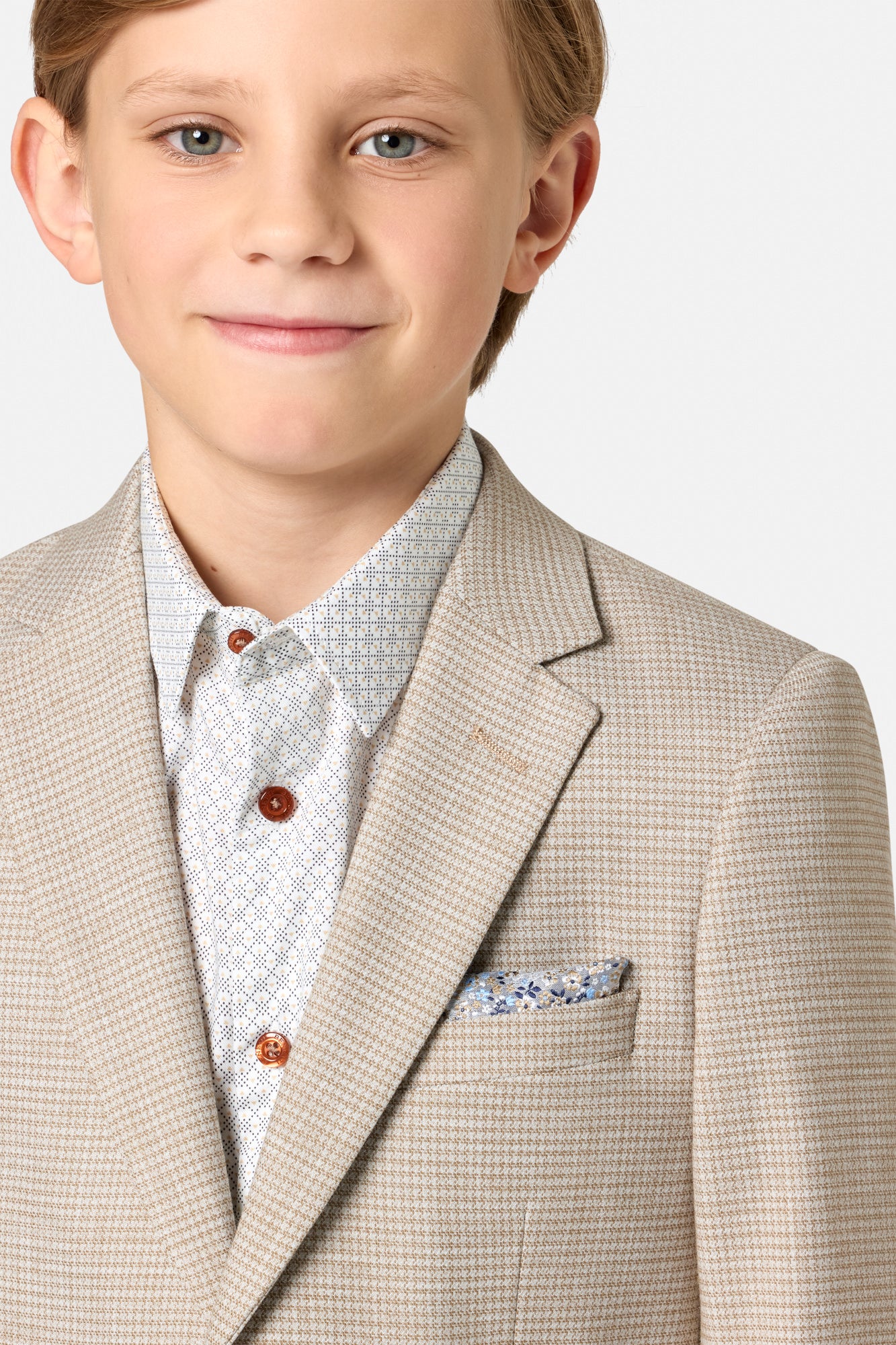 Young boy wearing a beige checkered suit with a white shirt and patterned tie on a light gray background