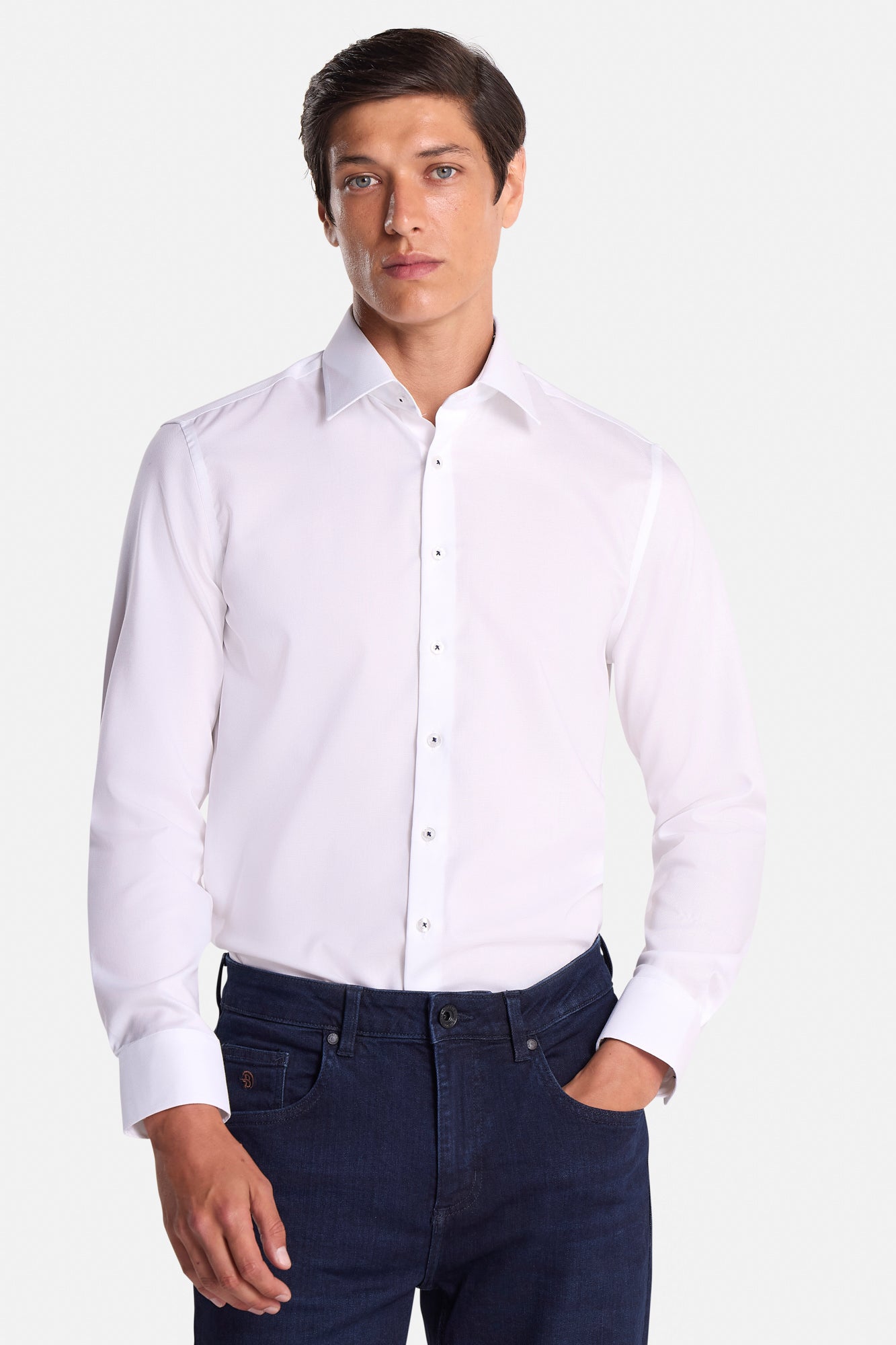 Man wearing a white dress shirt and dark jeans on a white background