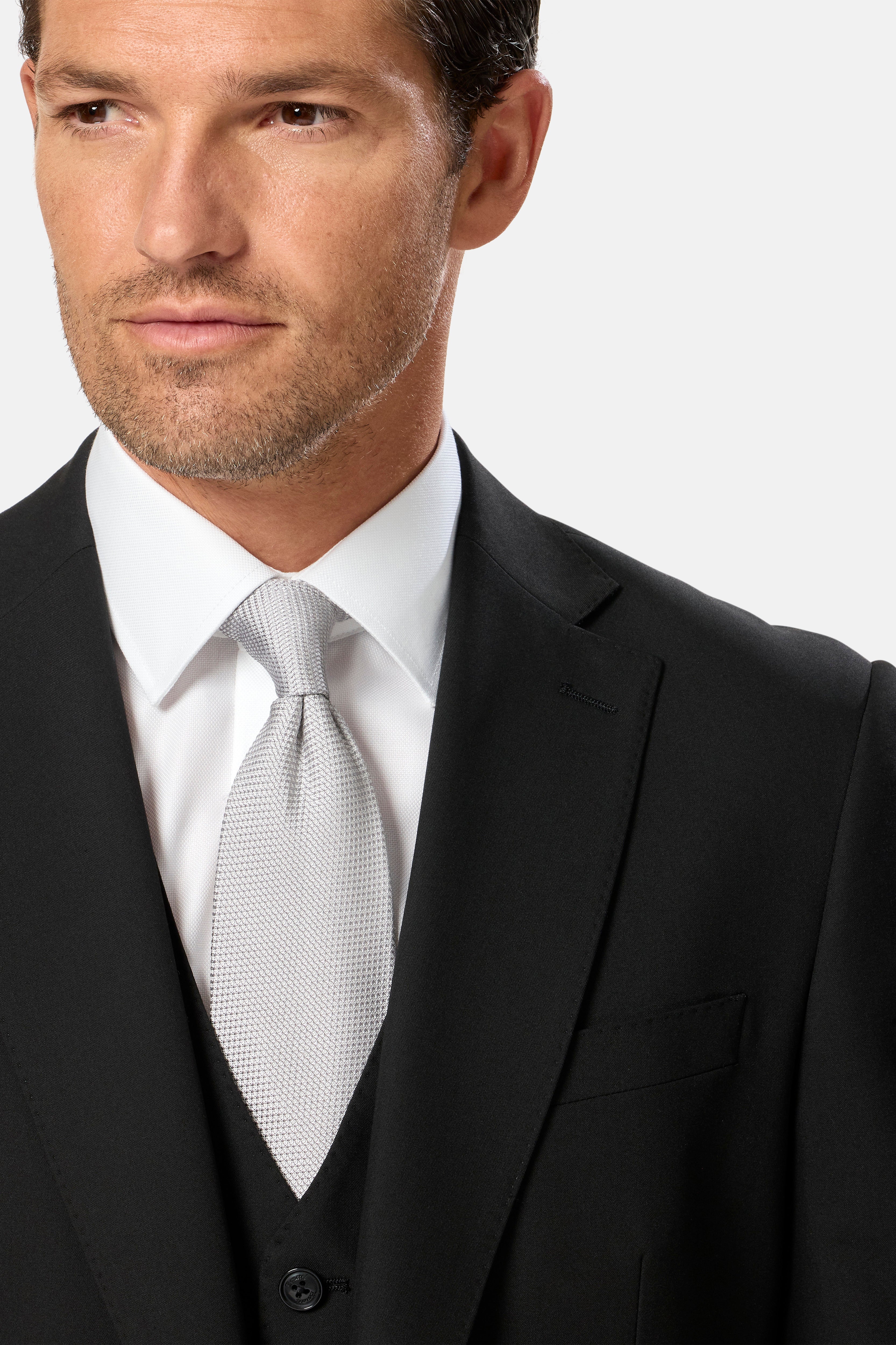 Man wearing a black suit with a white shirt and silver tie on a light gray background