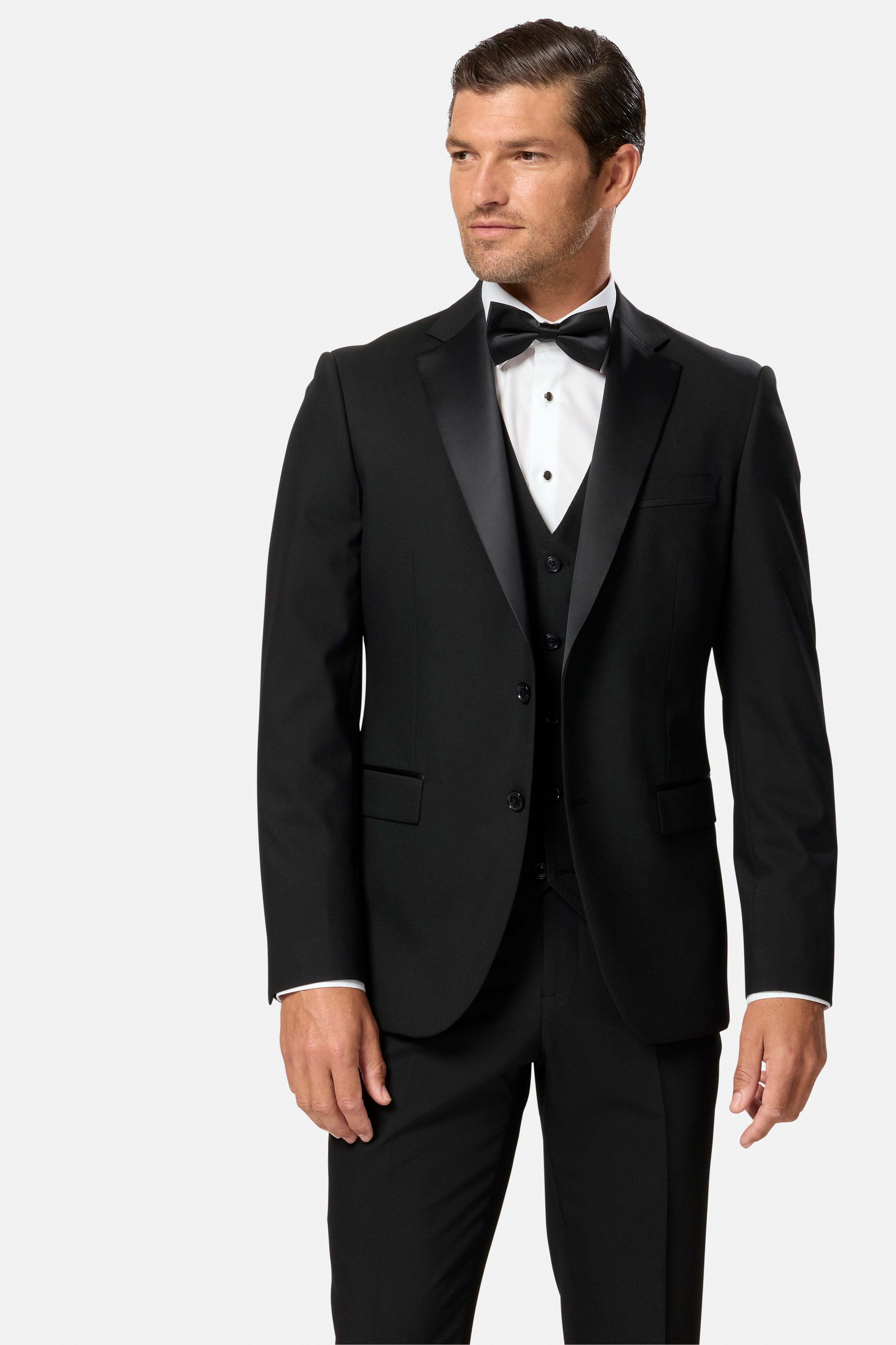 Man wearing a black tuxedo and black waistcoat with a white shirt and bow tie on a light gray background