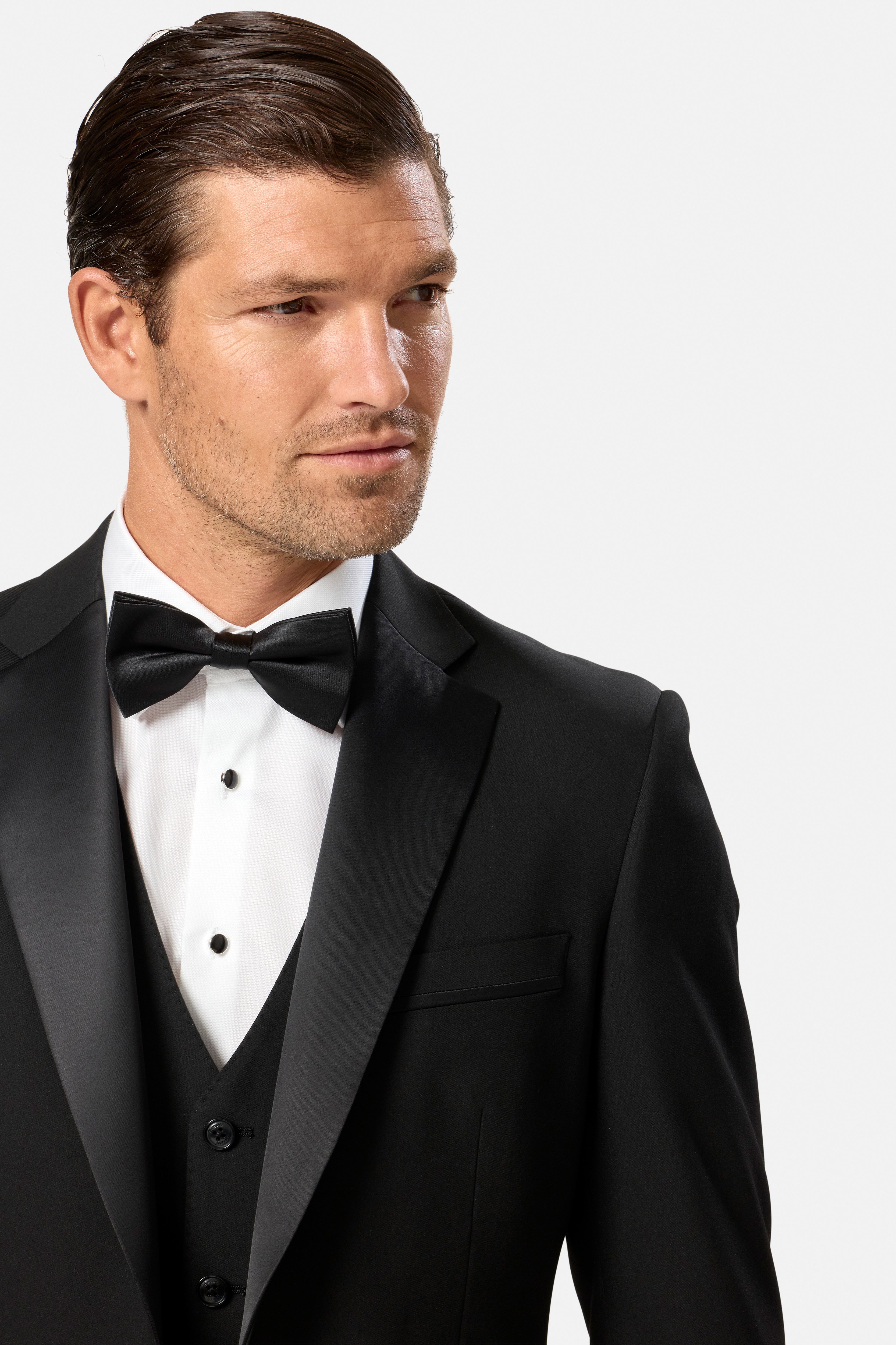Man wearing a black tuxedo black waistcoat with a bow tie on a white background