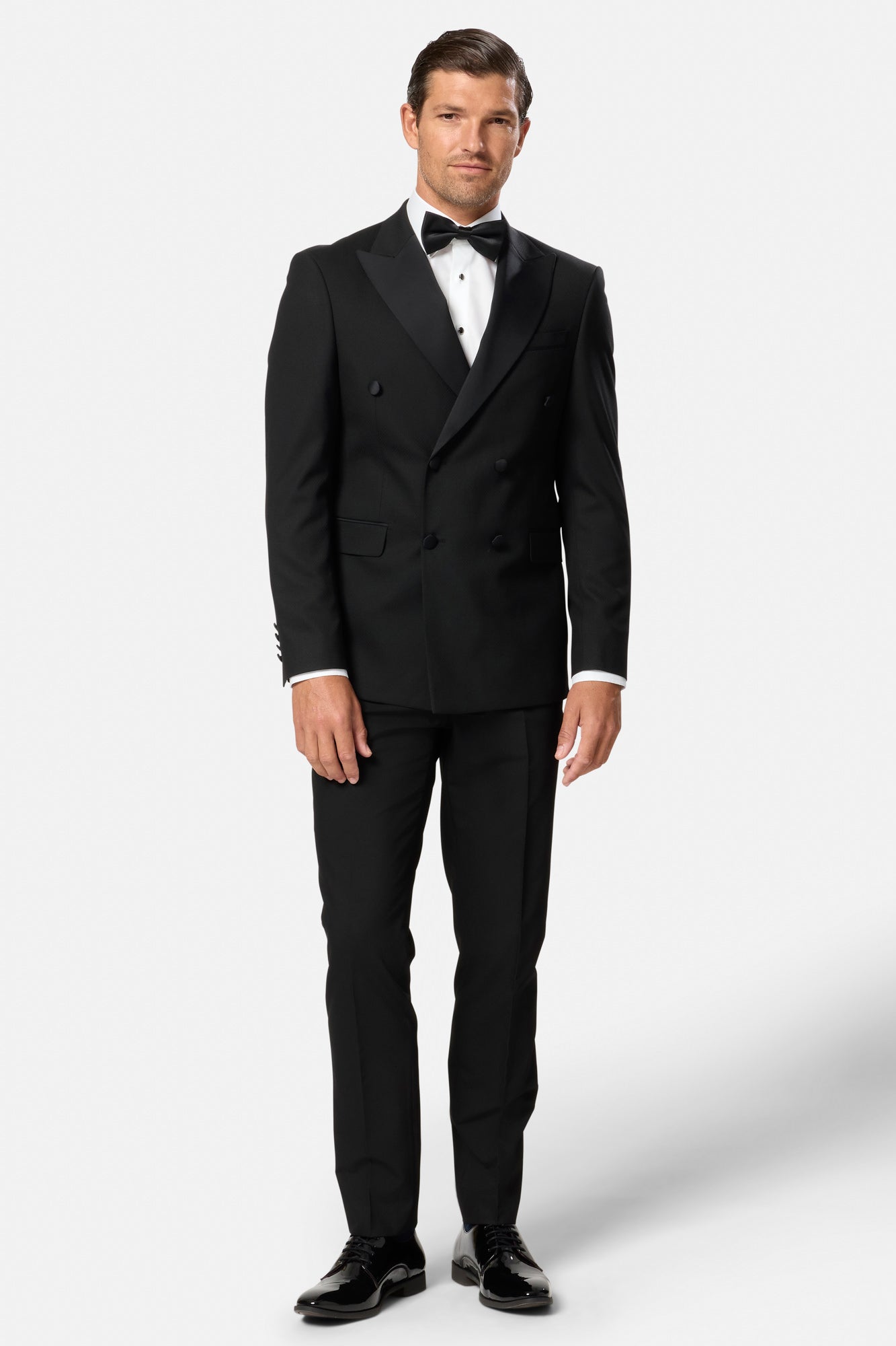 Man wearing a black double breasted tuxedo with a white shirt and black bow tie on a white background