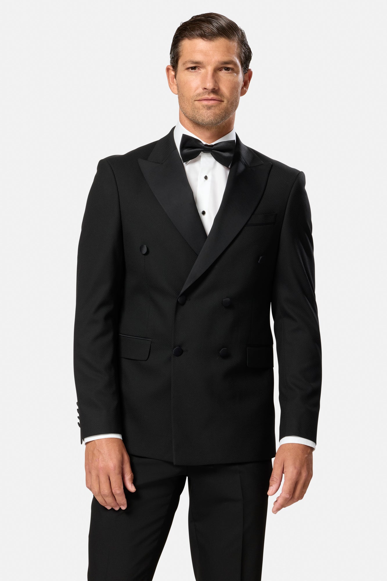 Man wearing a black double breasted tuxedo with a bow tie on a white background