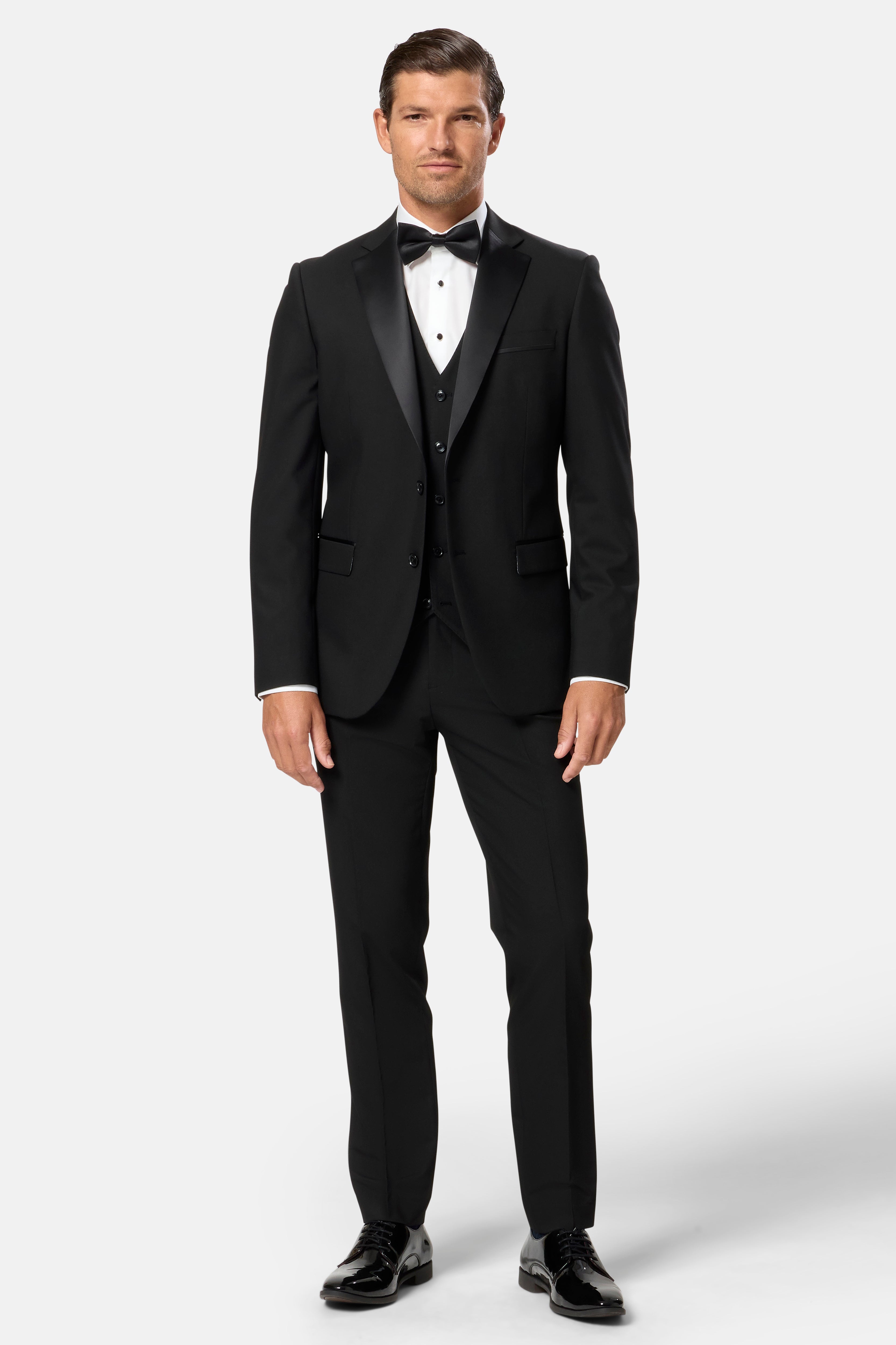 Man wearing a black tuxedo with a bow tie on a white background
