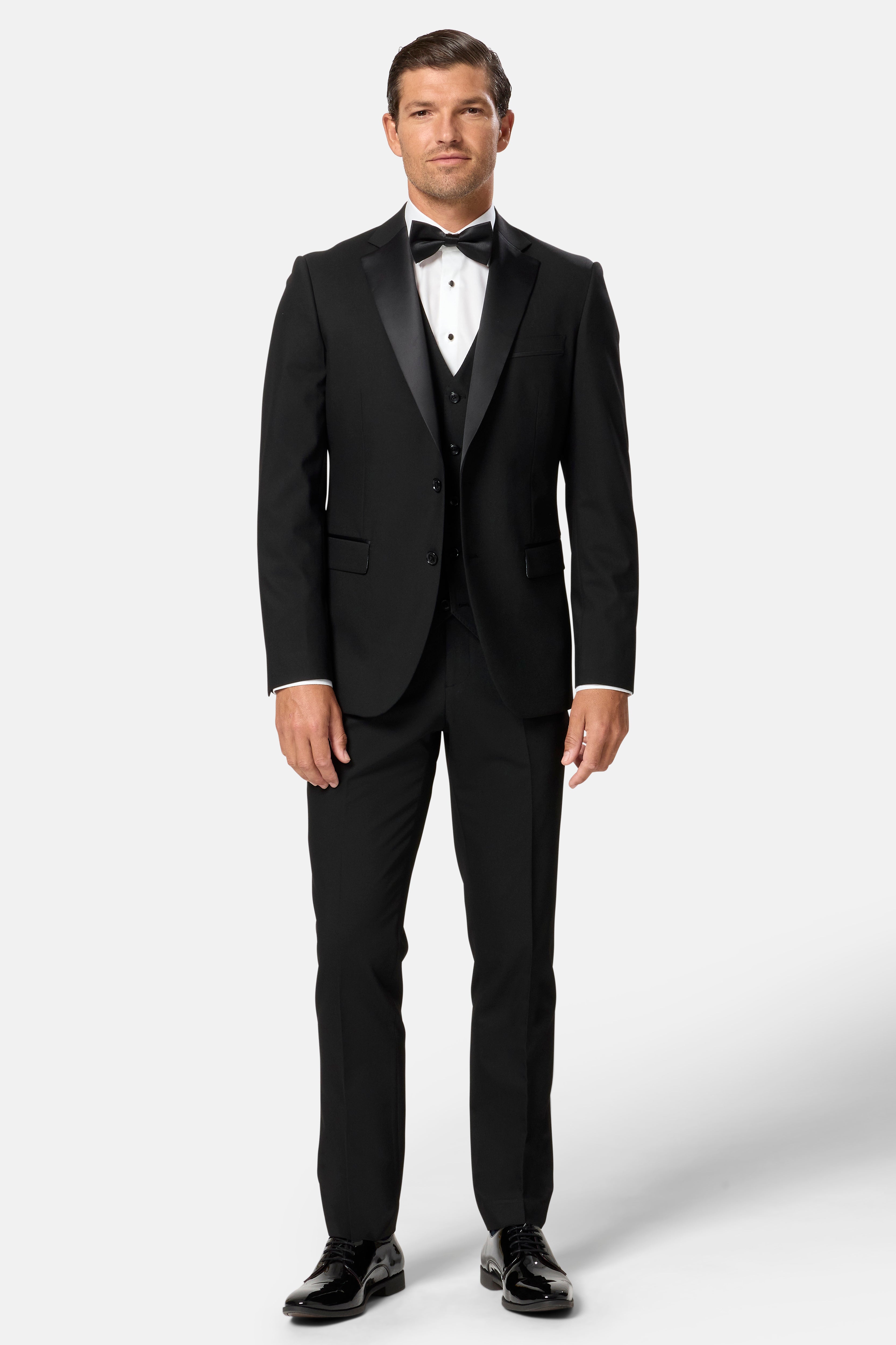 Man wearing a black tuxedo with a white shirt and black bow tie on a white background