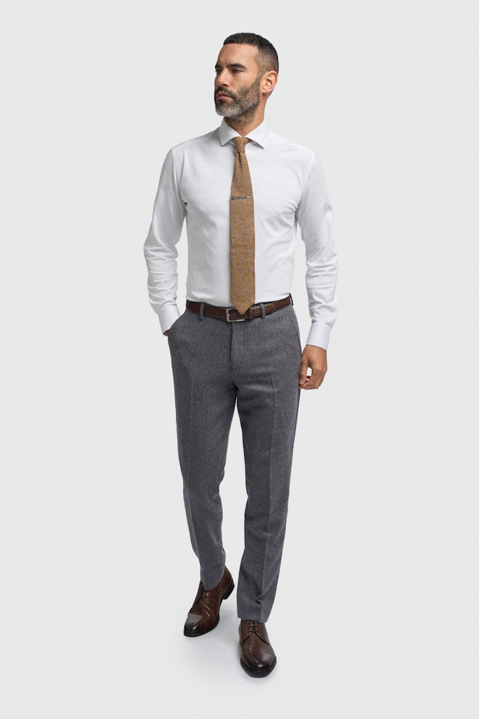Man wearing a white dress shirt, brown tie, gray pants, and brown shoes on a white background