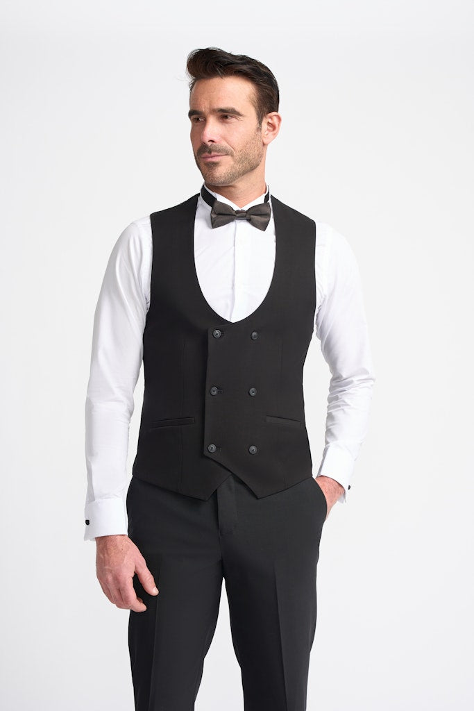 Man wearing a black double breasted waistcoat over a white shirt with a bow tie on a white background