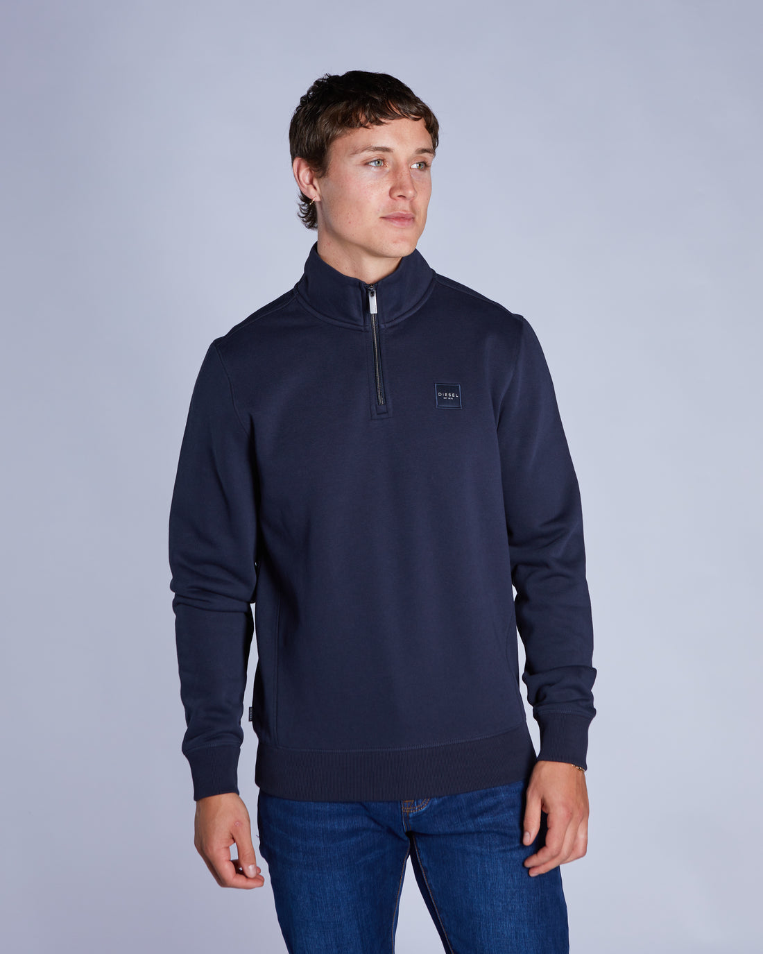 Man wearing a navy blue quarter-zip sweater with a brand logo on a light gray background
