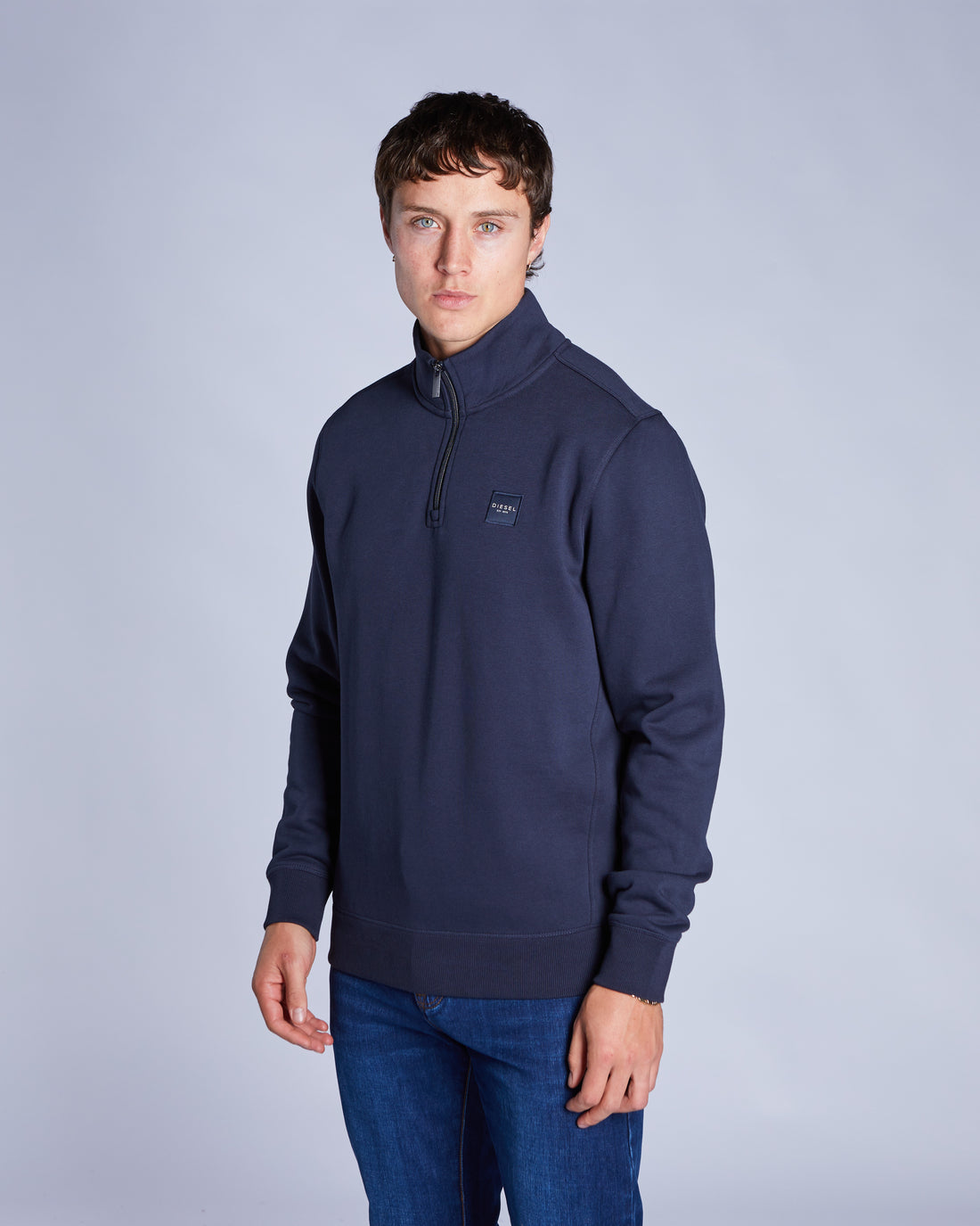 Man wearing a navy blue pullover with a brand logo on a light gray background