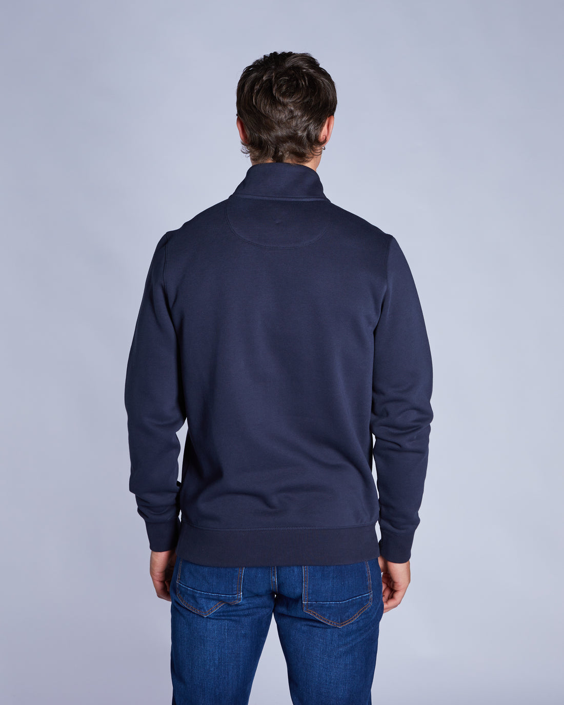 Man wearing a navy blue swaet on a gray background