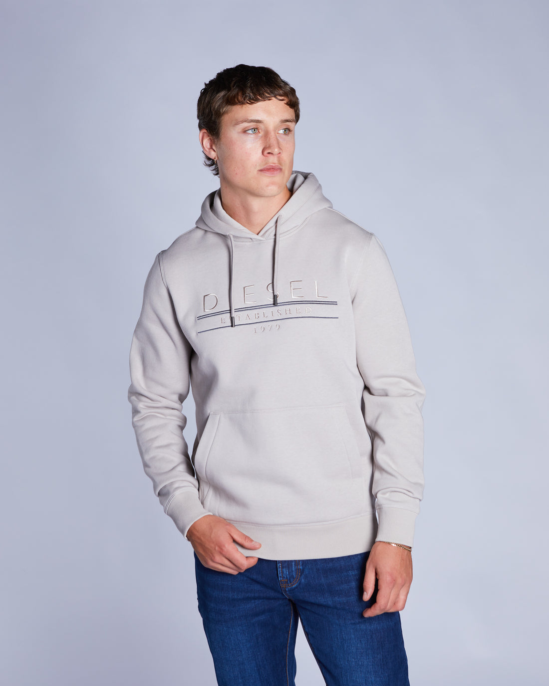 Man wearing a beige  hoodie with a brand logo on a plain background