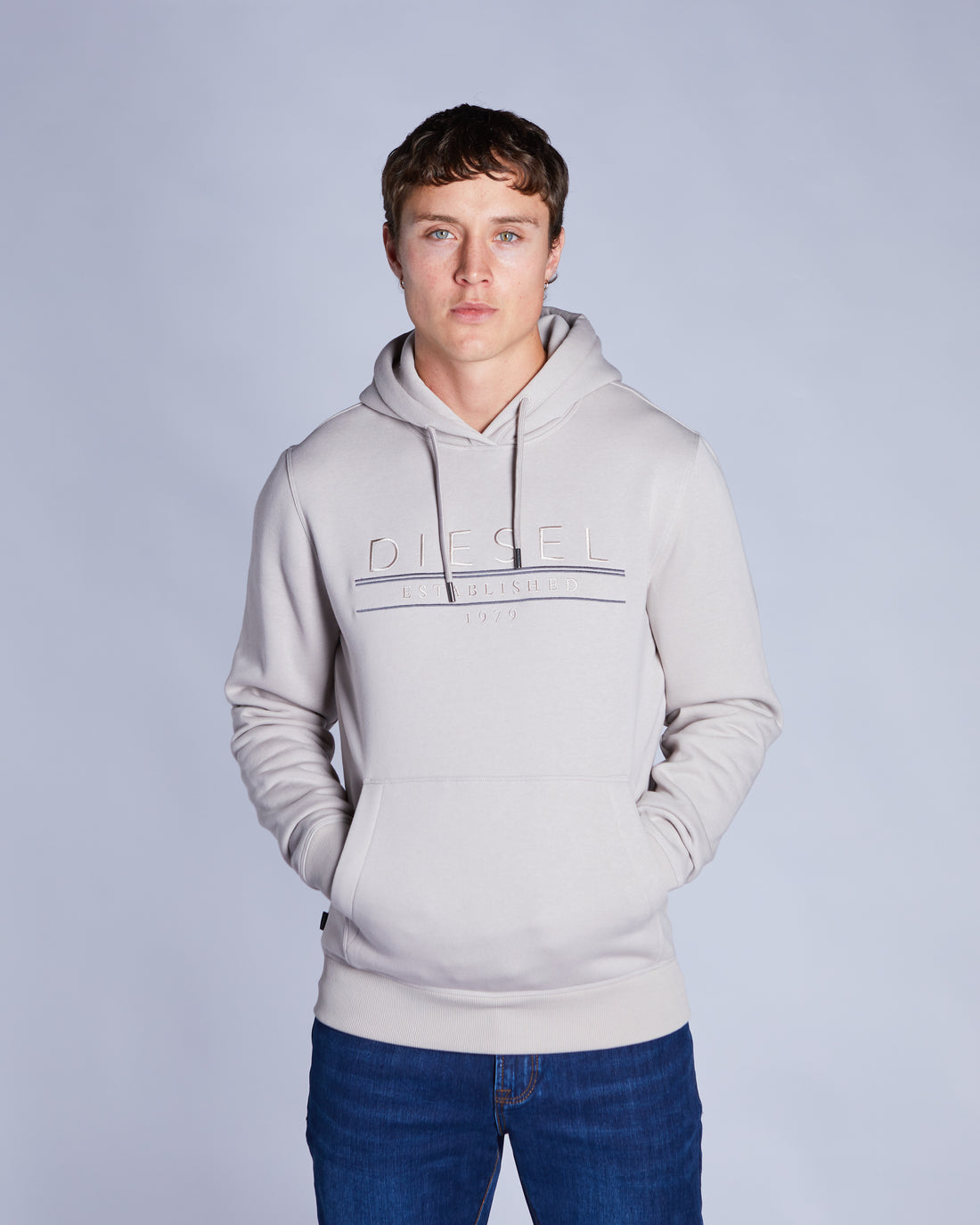 Man wearing a beige  hoodie with a brand logo on a light gray background