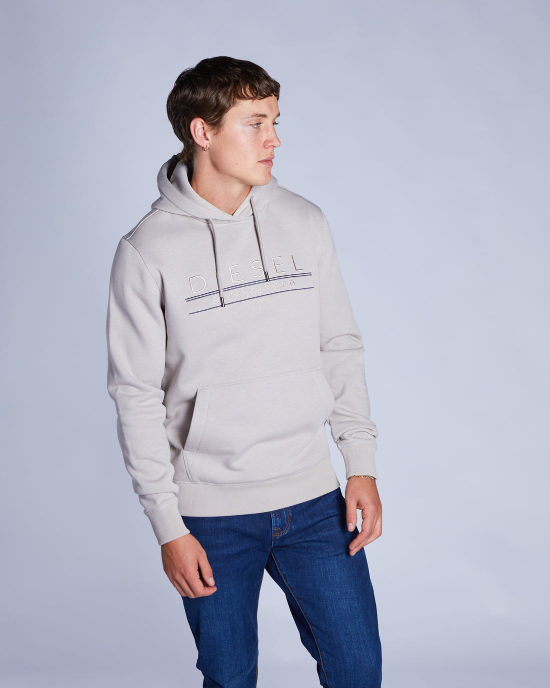 Person wearing a beige  hoodie and blue jeans on a plain background