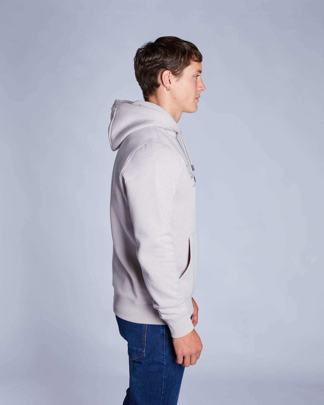 Person wearing a beige  hoodie and blue jeans against a plain background