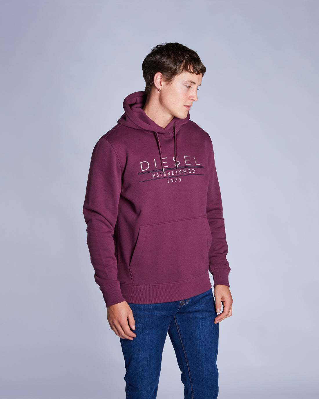 Person wearing a maroon Diesel hoodie on a light gray background