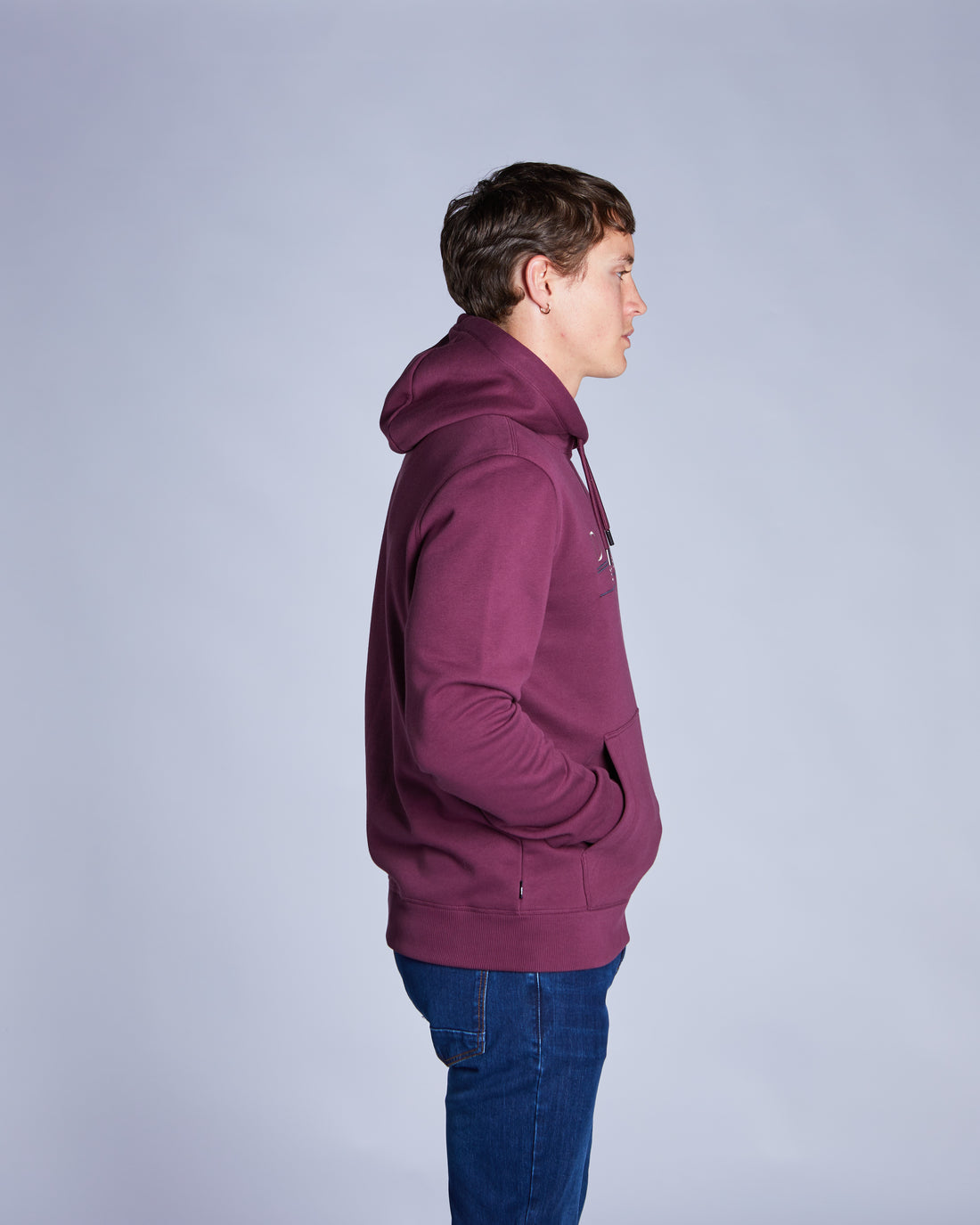Person wearing a maroon hoodie and blue jeans on a light gray background