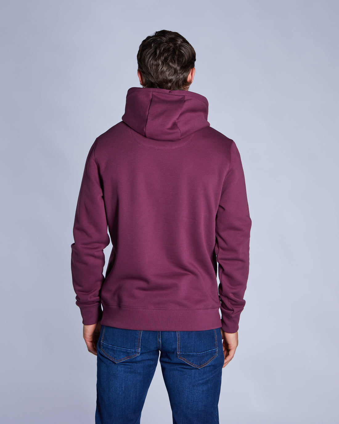 Person wearing a maroon hoodie and blue jeans on a gray background