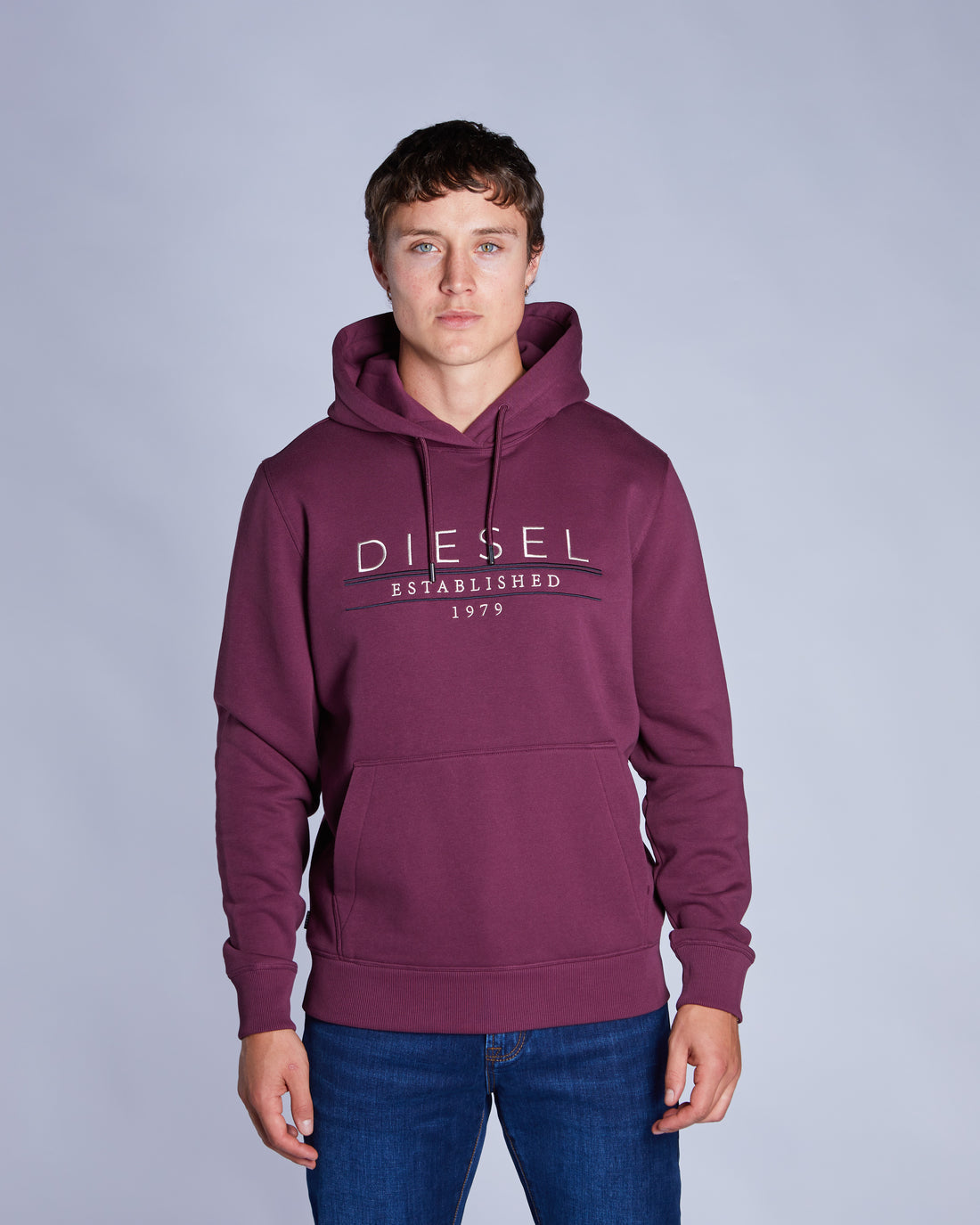 Person wearing a maroon hoodie with Diesel logo on a gray background