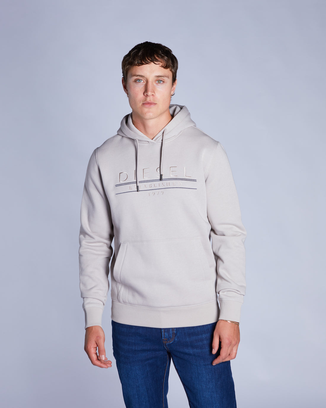 Person wearing a beige hoodie with a brand logo on a plain background