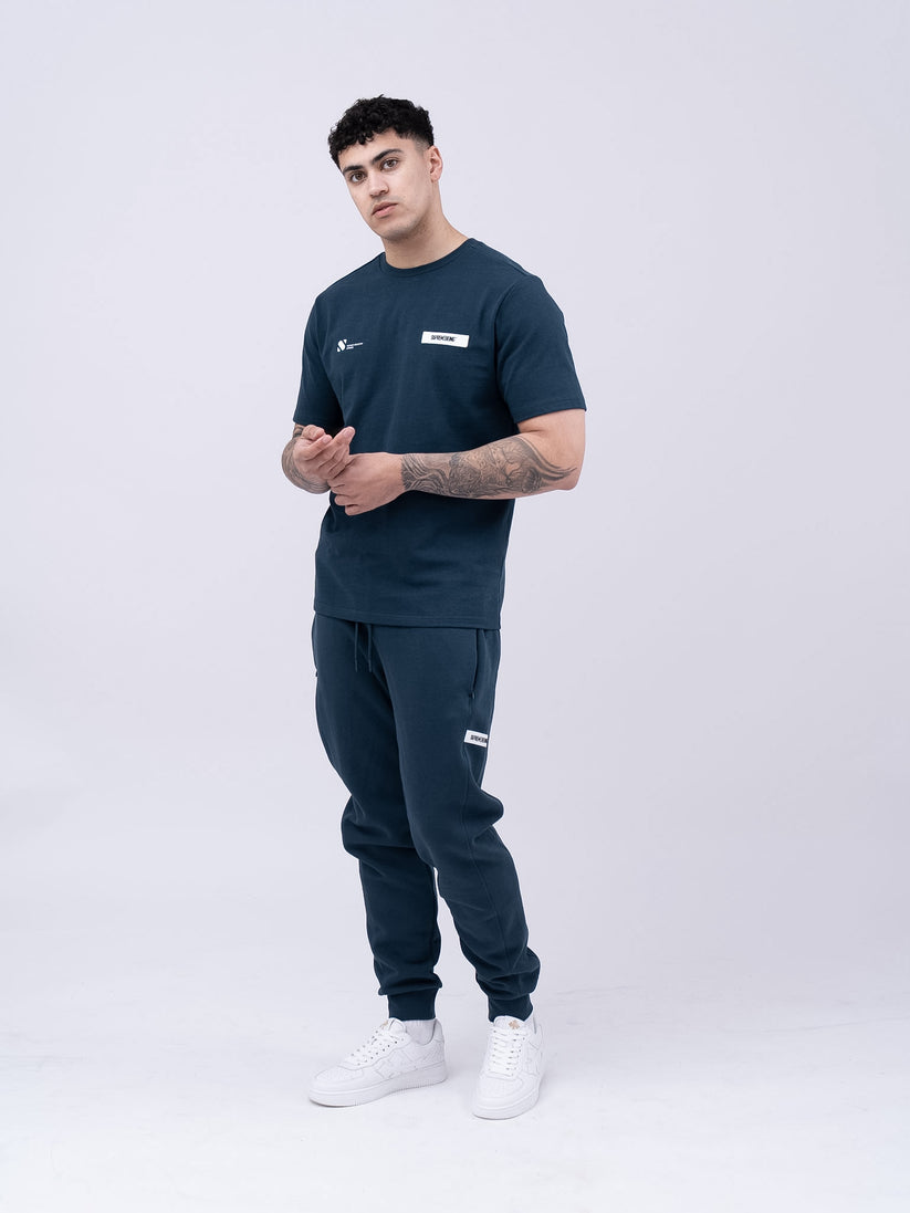 Man wearing navy Reso Tee with brand logos on a white background