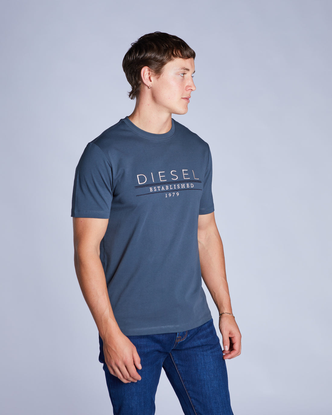 Man wearing a petrol blue tee and blue jeans standing sideways