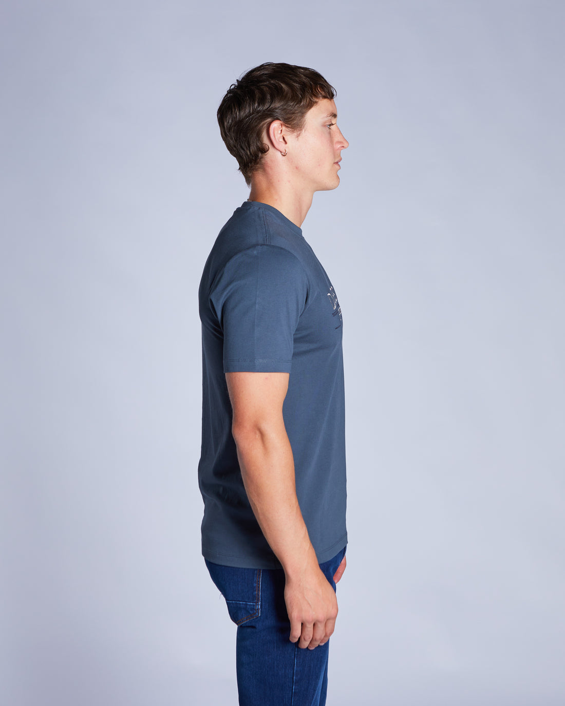 Man wearing a petrol blue tee and blue jeans side view