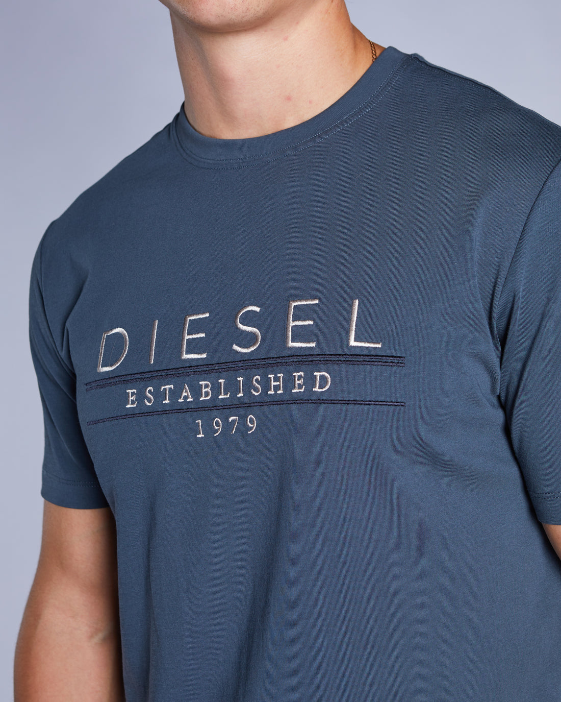 Man wearing a petrol blue tee and blue jeans chest logo close up