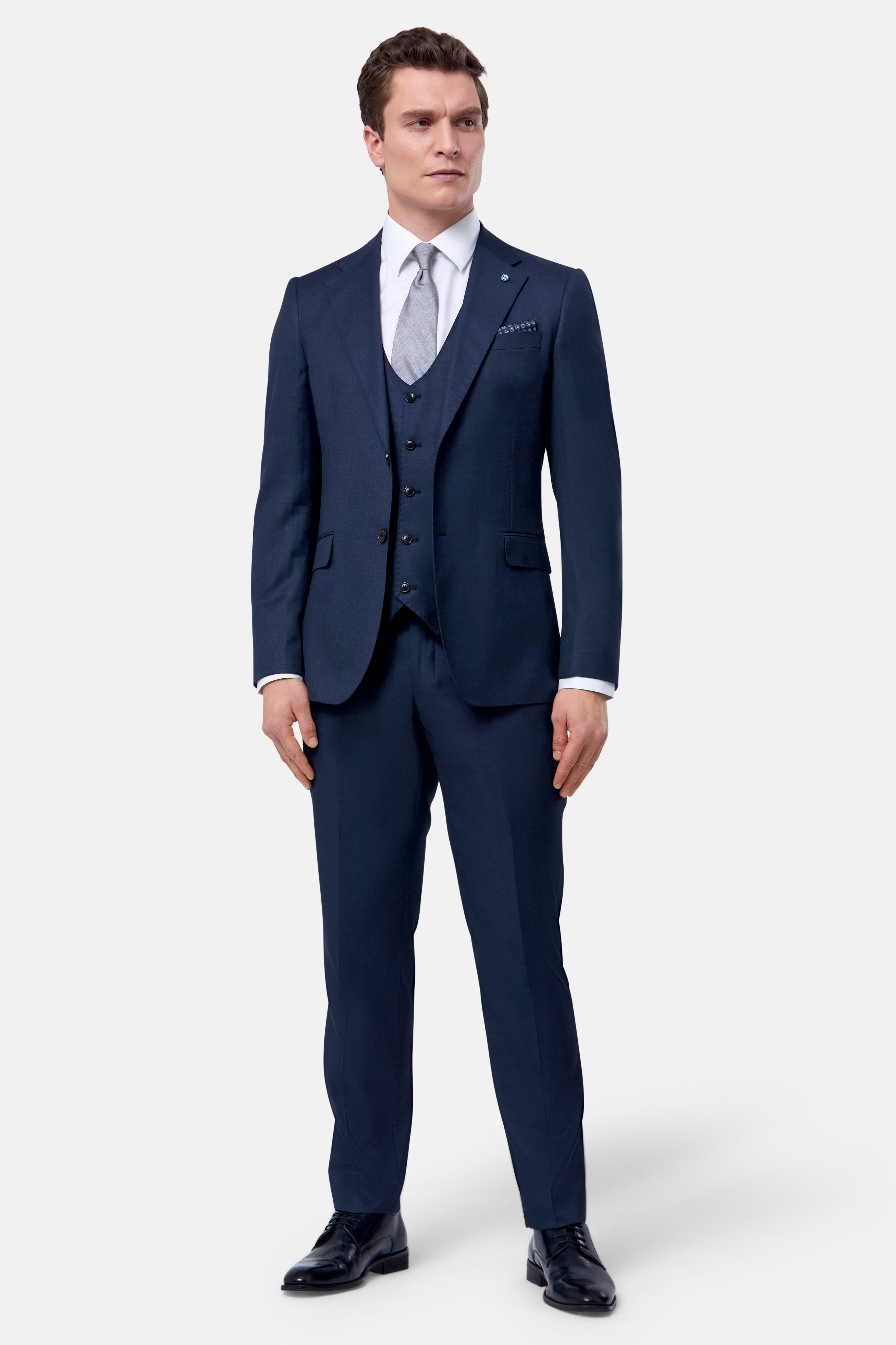 Man wearing a navy blue suit with a white shirt and black shoes on a white background