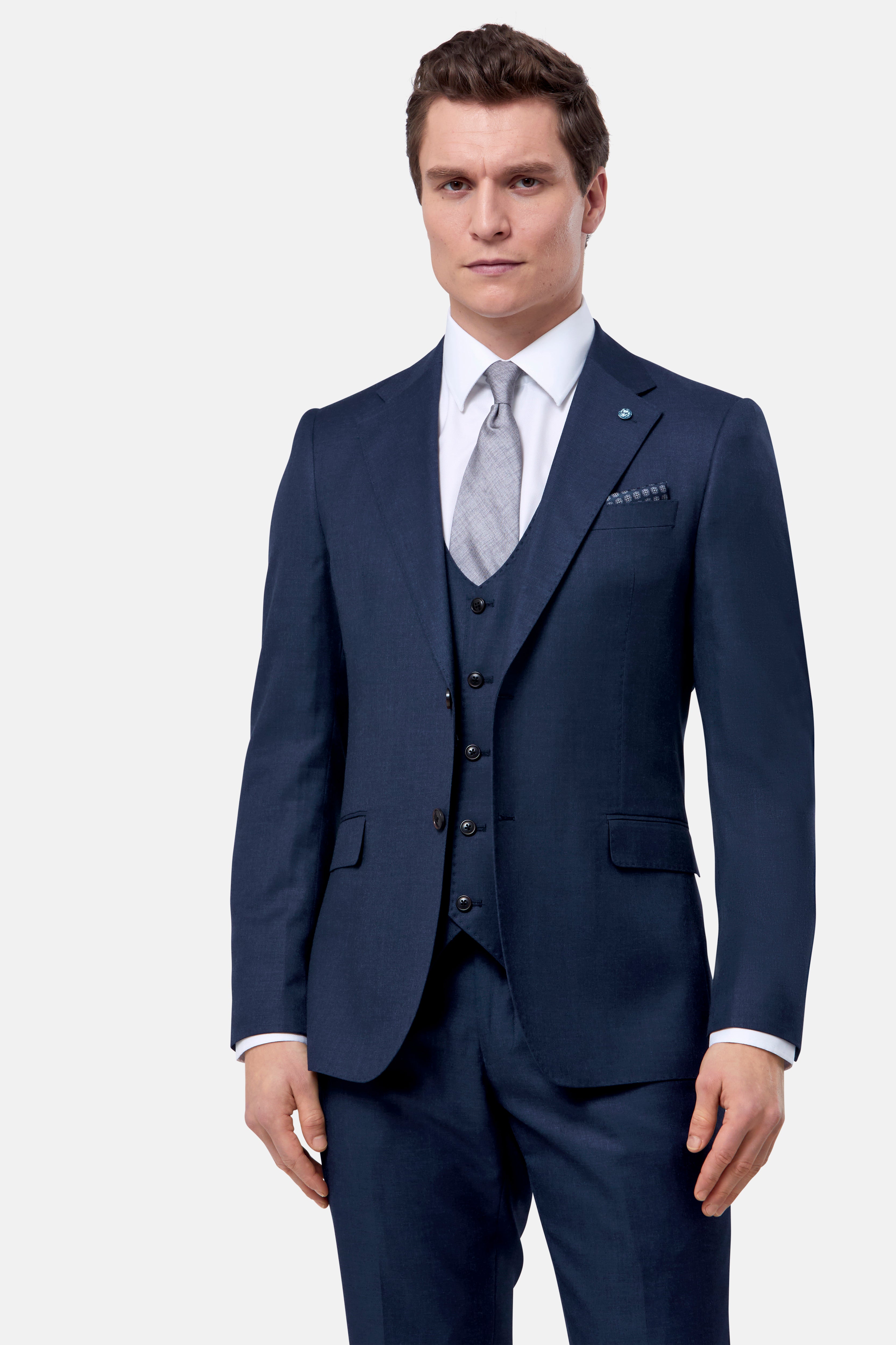 Man wearing a navy blue suit with a white shirt and gray tie on a light gray background