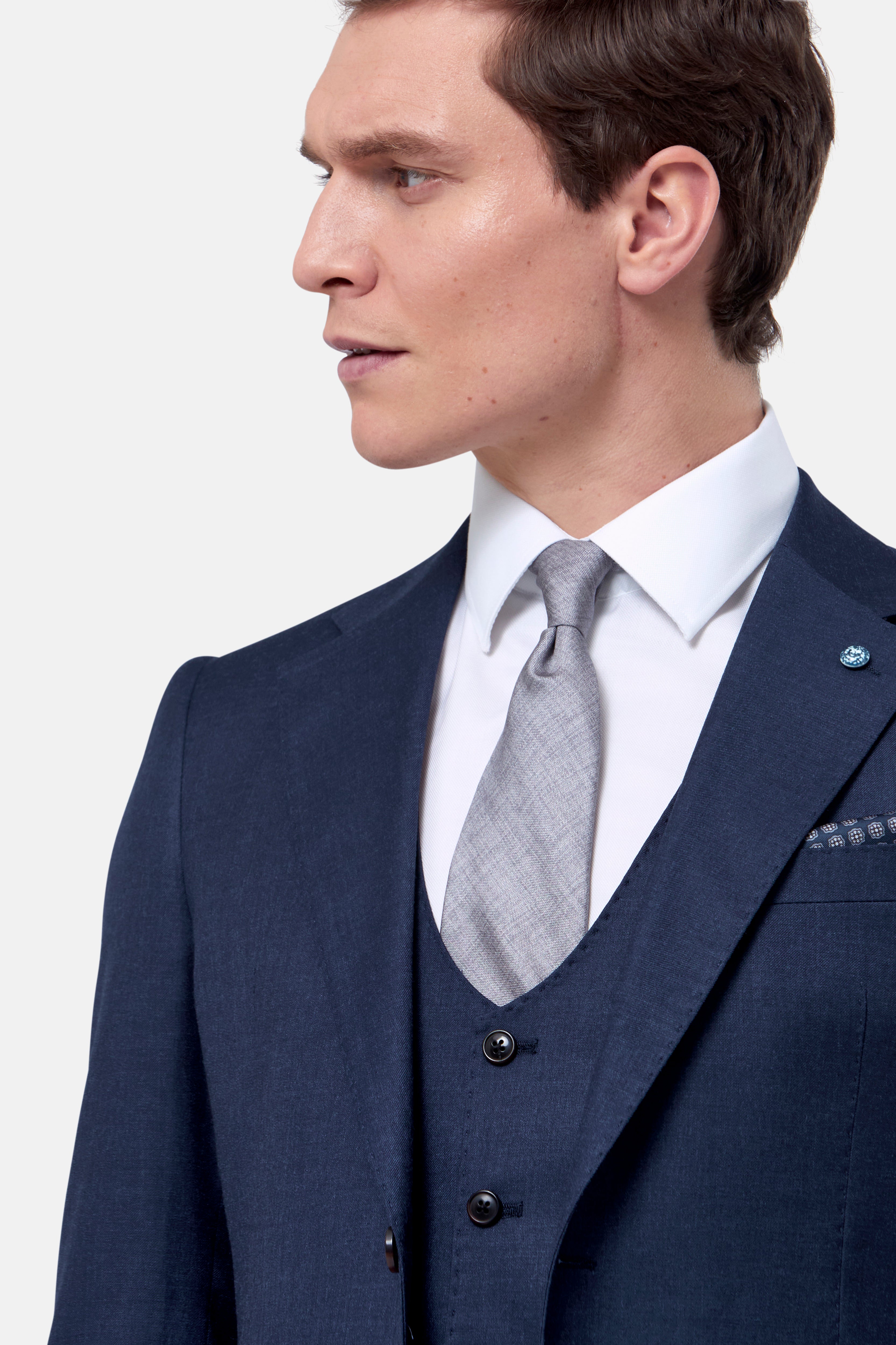 Man wearing a navy suit with a white shirt and gray tie on a light gray background