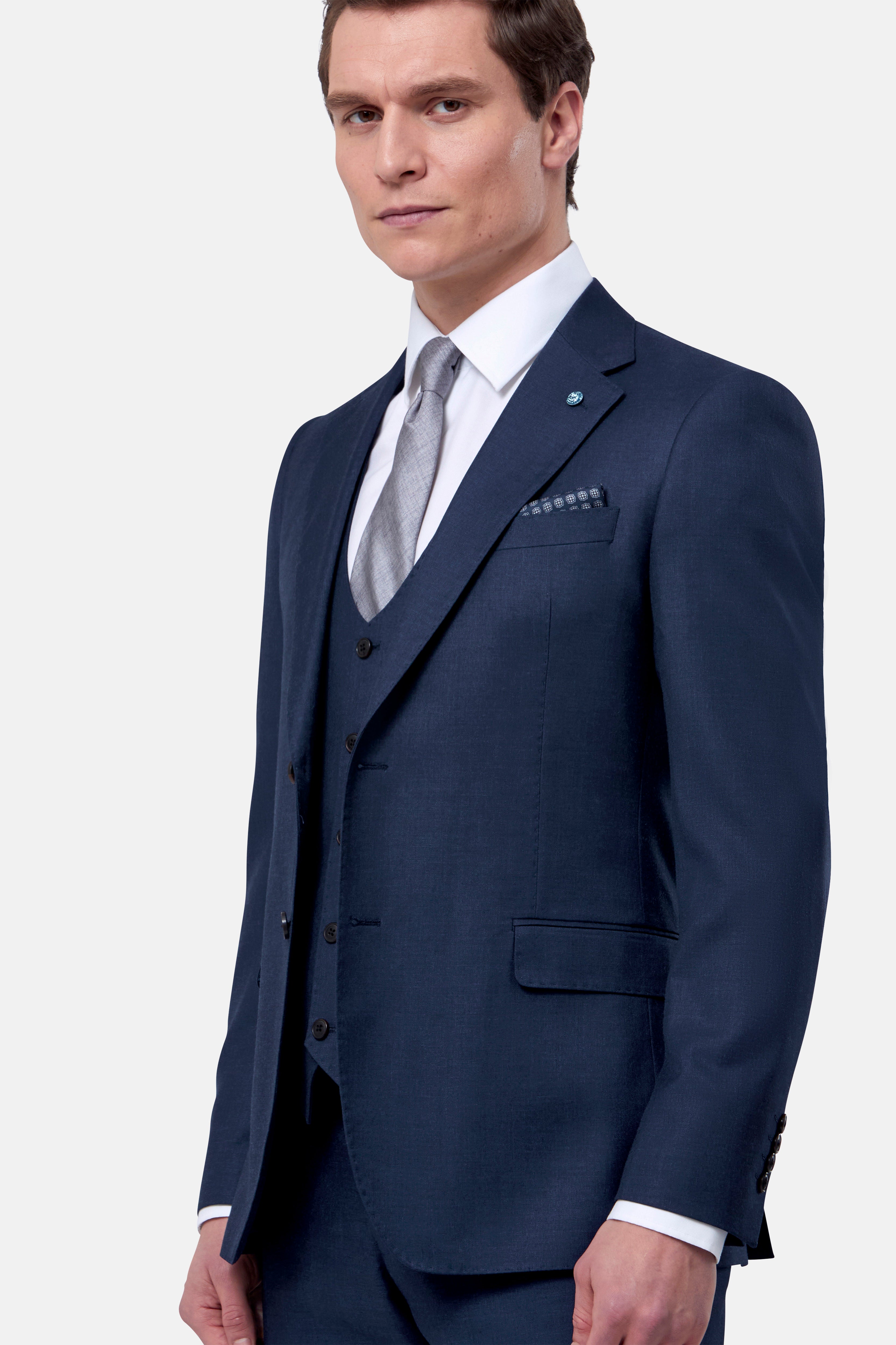 Man wearing a navy blue suit with a white shirt and gray tie on a light gray background