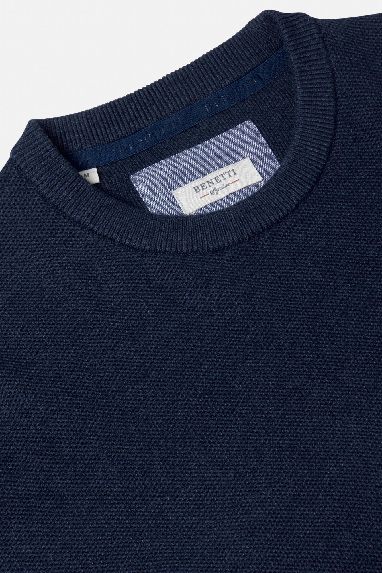 Close-up of a navy sweater with a brand label on a light gray background