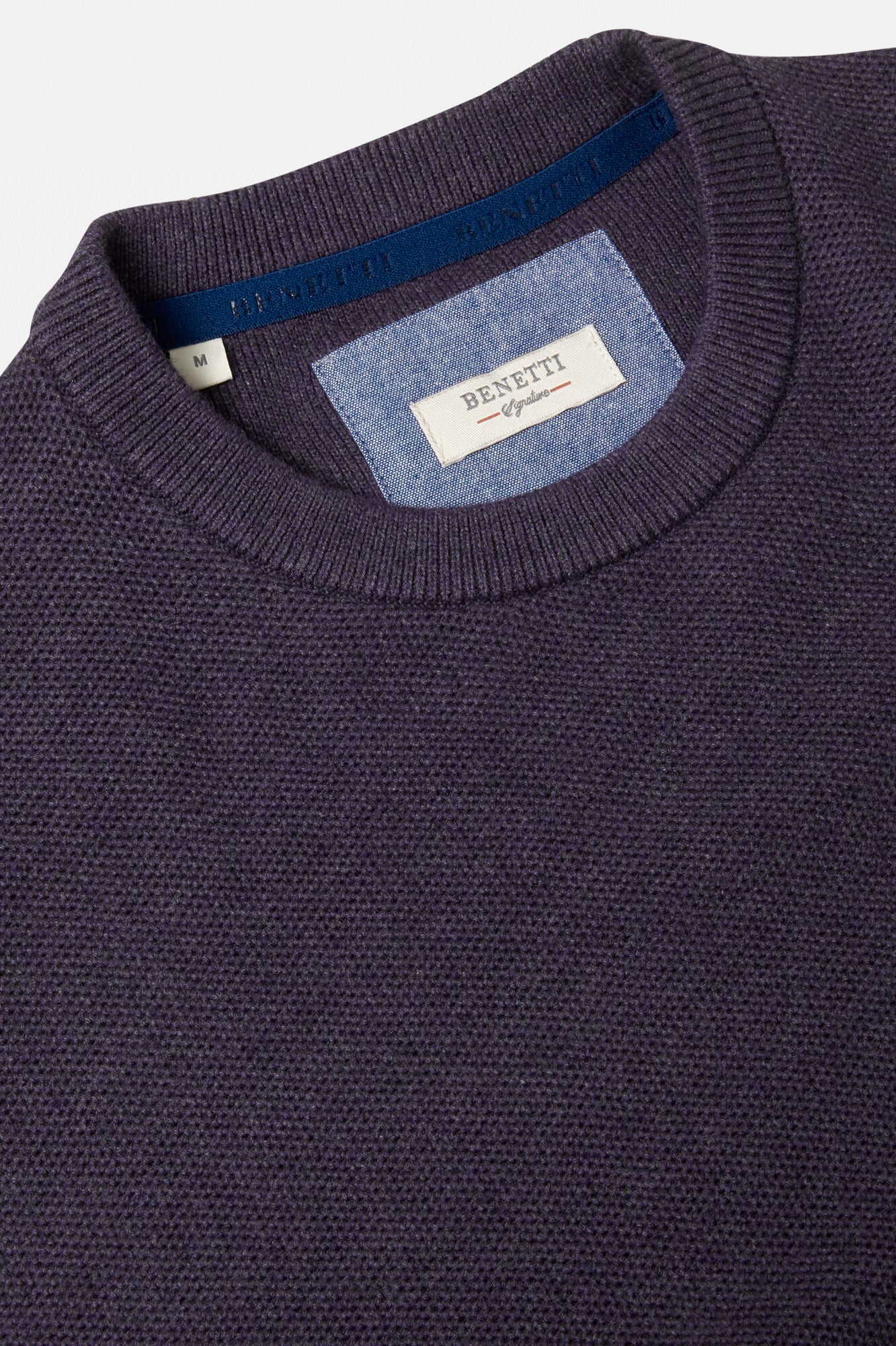 Close-up of a grape sweater with a brand label on a light gray background