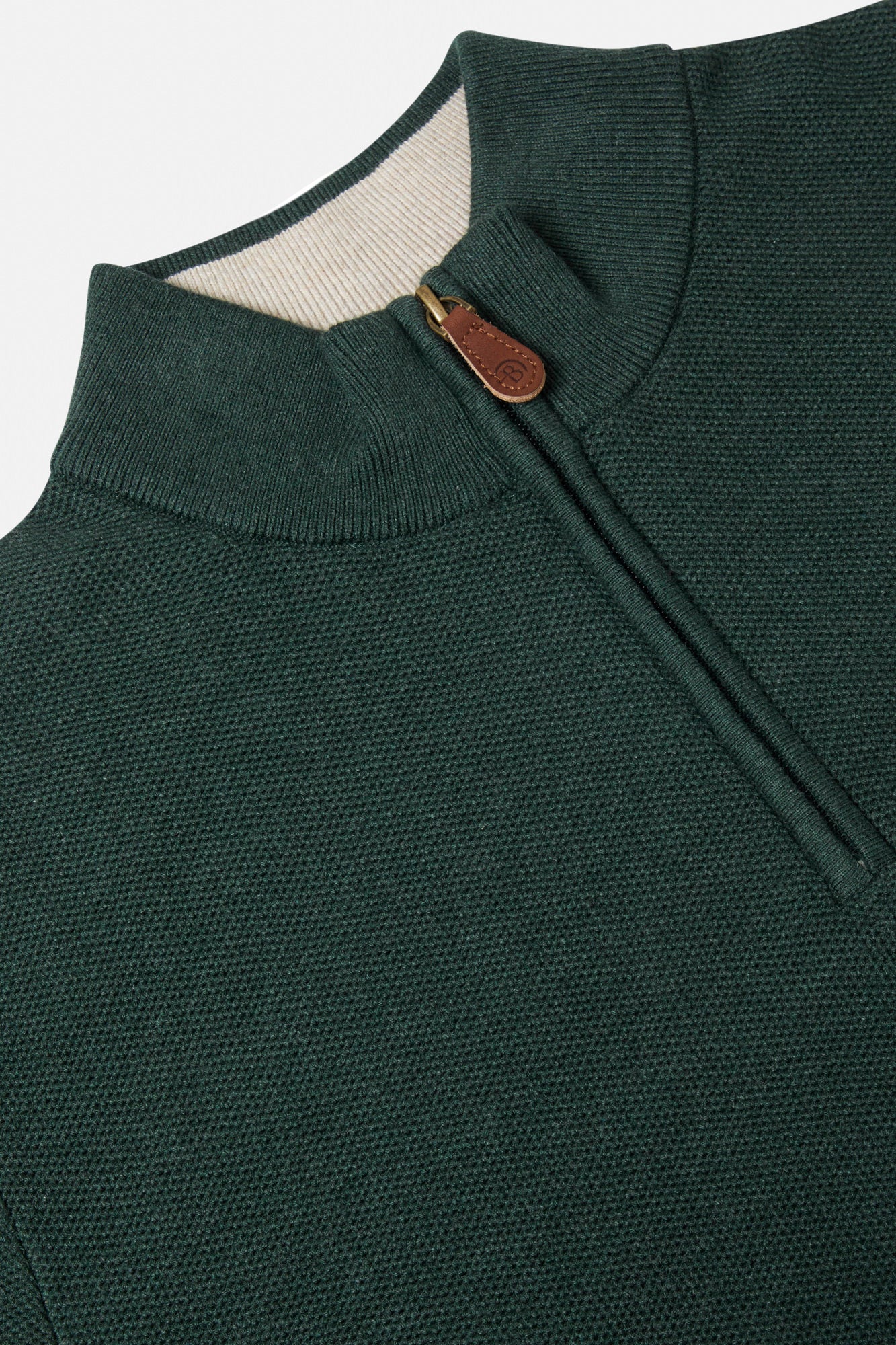 Close-up of a green sweater with a zipper and brown leather pull tab on a light gray background