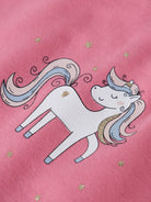 A close-up of a pink fabric featuring a cartoon unicorn graphic with pastel blue and pink hair, gold stars, and a small gold heart on the side.