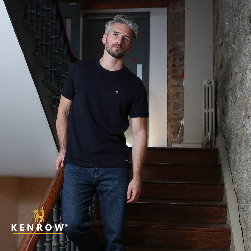Man standing on a staircase wearing a black t-shirt and blue jeans, with 'KENROW' branding visible.
