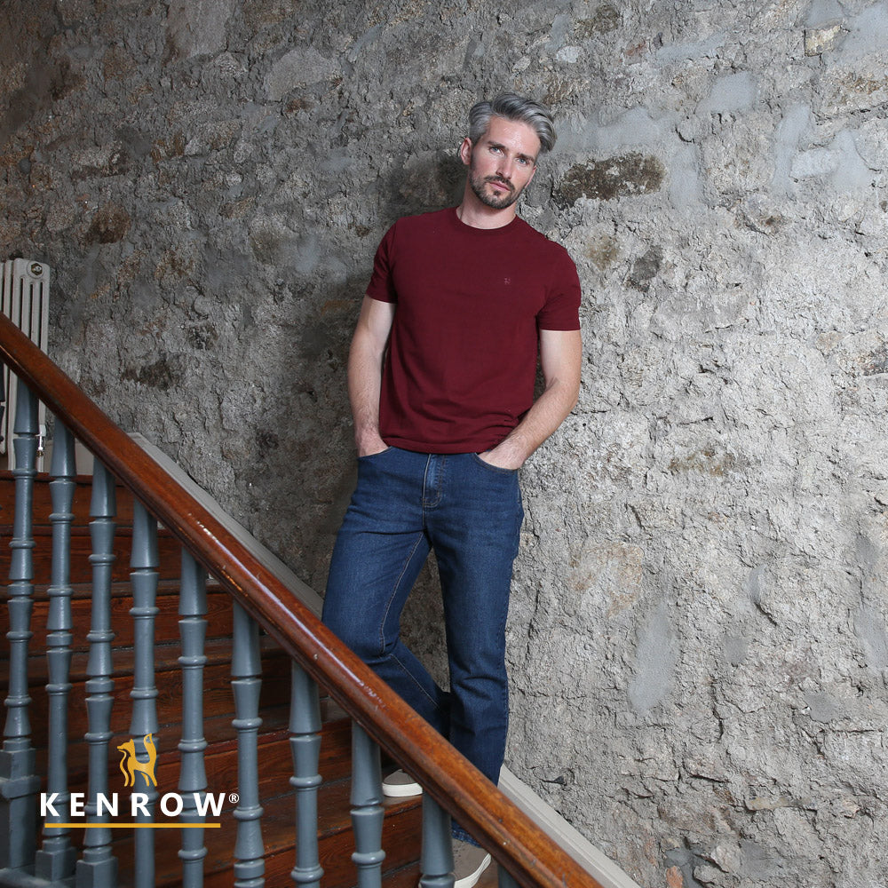 Man in a red shirt and blue jeans leaning against a stone wall with 'Kenrow' branding.