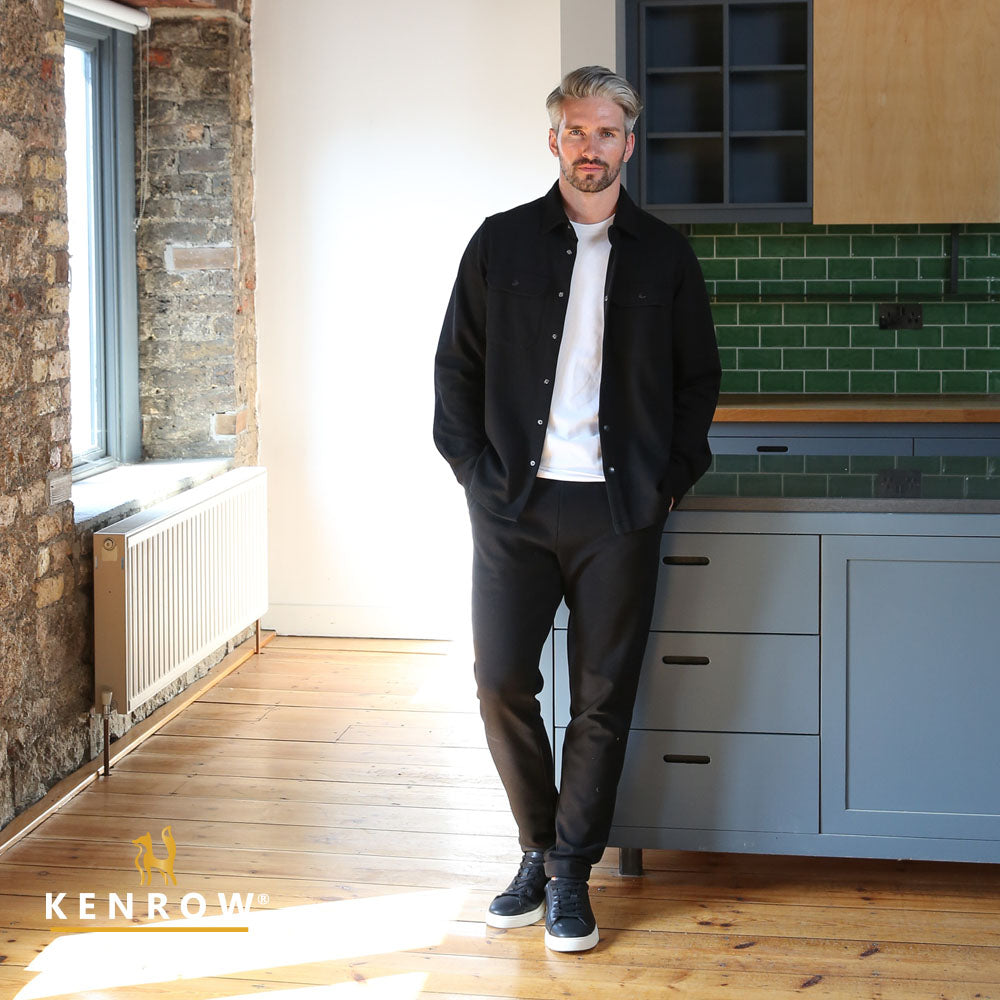 Man standing in a modern kitchen with green tiles and wooden floor in a white t-shirt