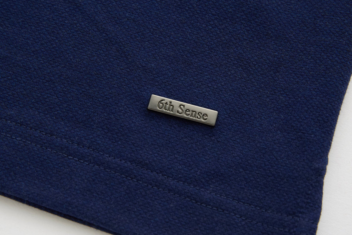 6th Sense metal logo badge on the lower hem of the Evoke dress blue polo