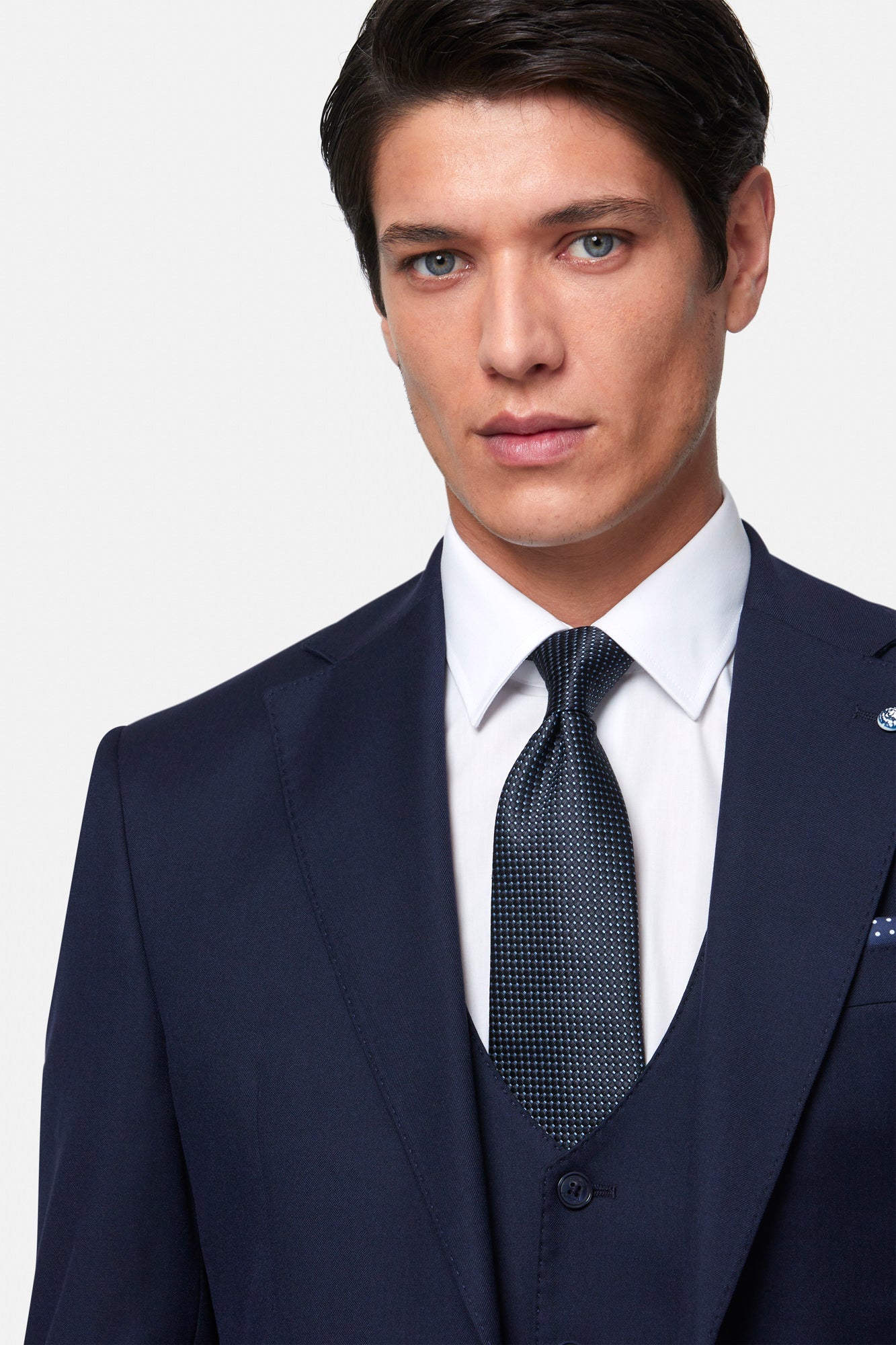 Man wearing a navy Benetti Edina suit with a white shirt and patterned tie on a light gray background