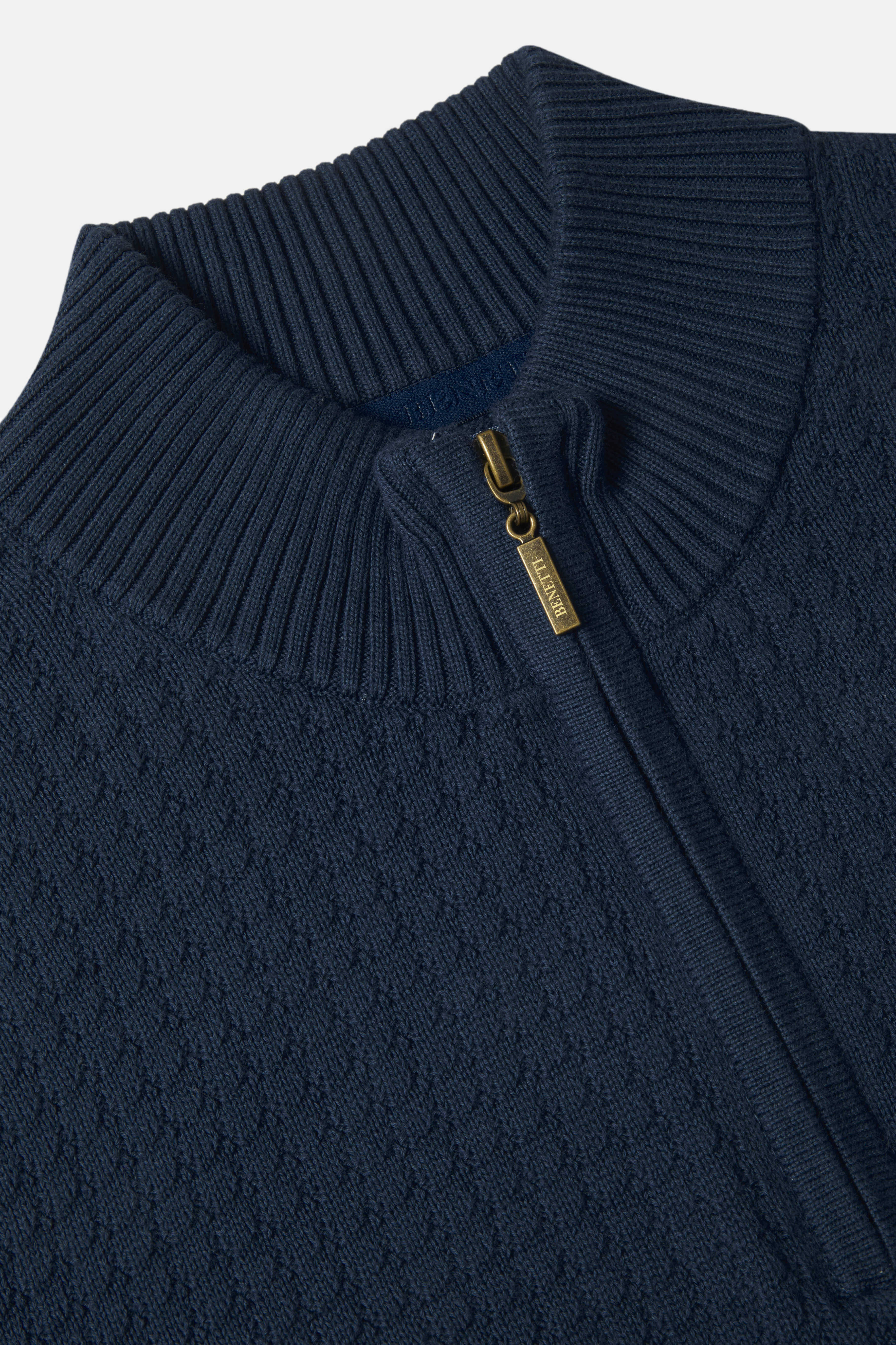 Indigo blue knitted sweater with a gold zipper detail on a light gray background