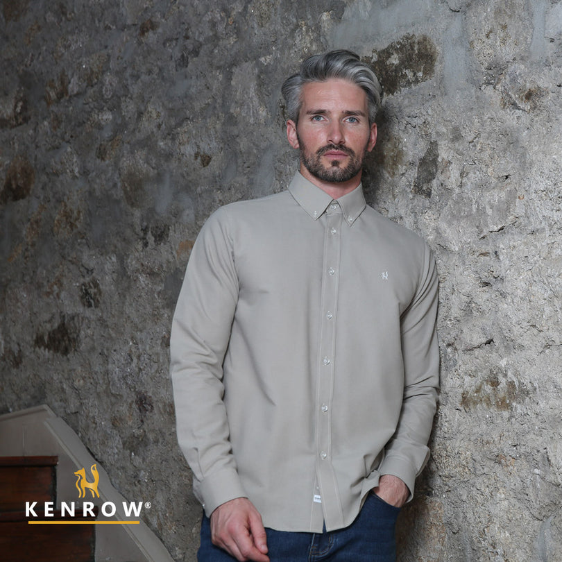 Close up of a man wearing a putty coloured shirt leaning against a stone wall