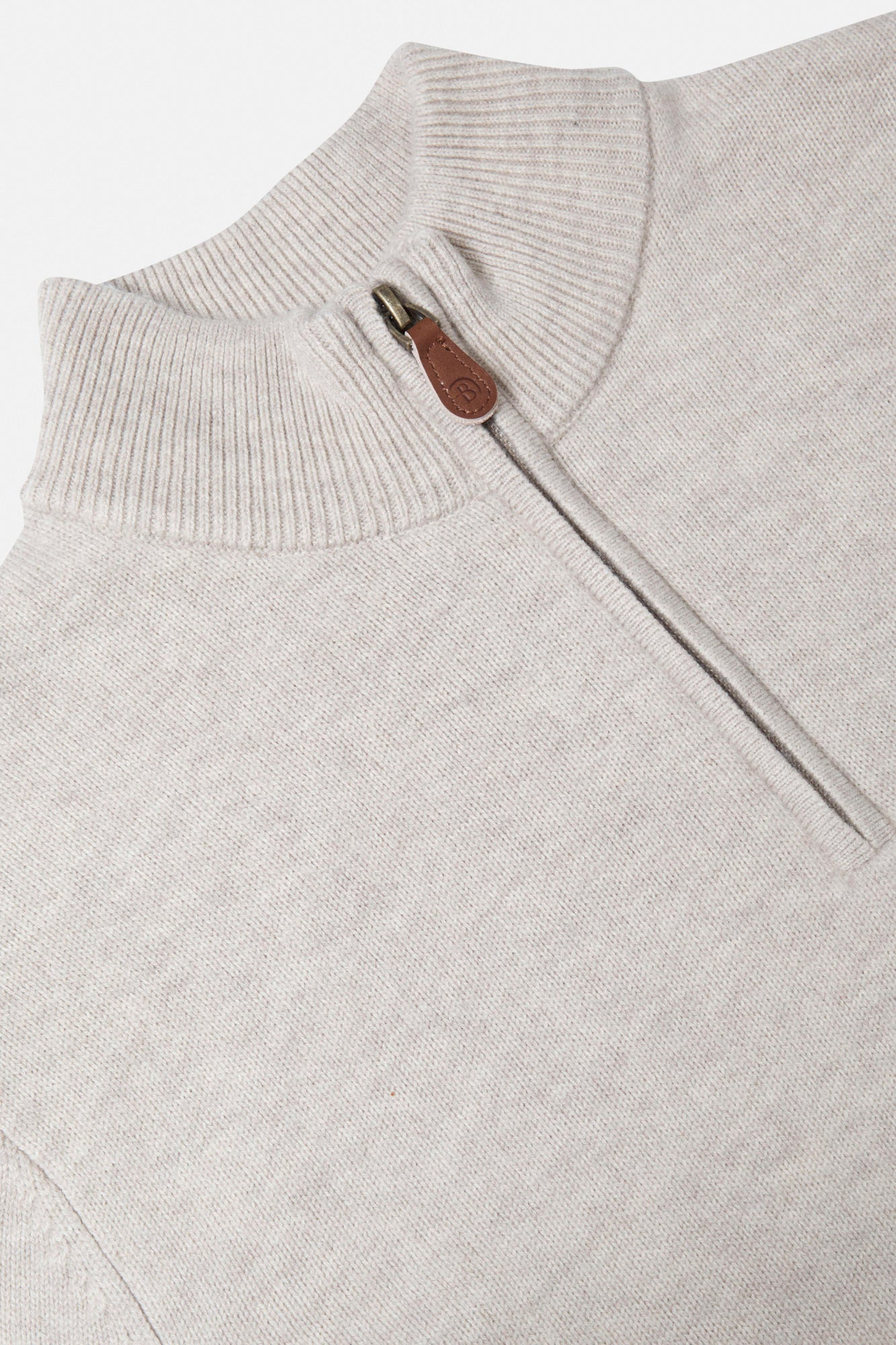 Close-up of a light beige sweater with a zipper and leather patch on a white background