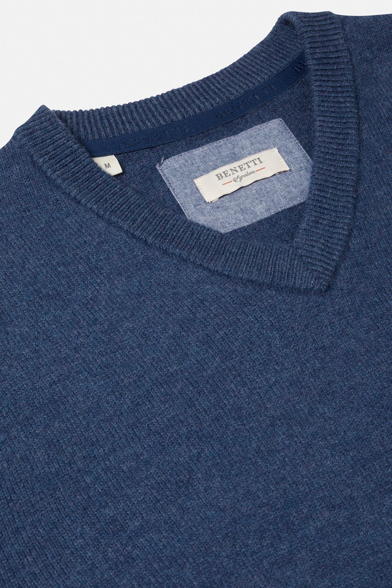 Close-up of a blue v-neck sweater with a brand label on a light gray background