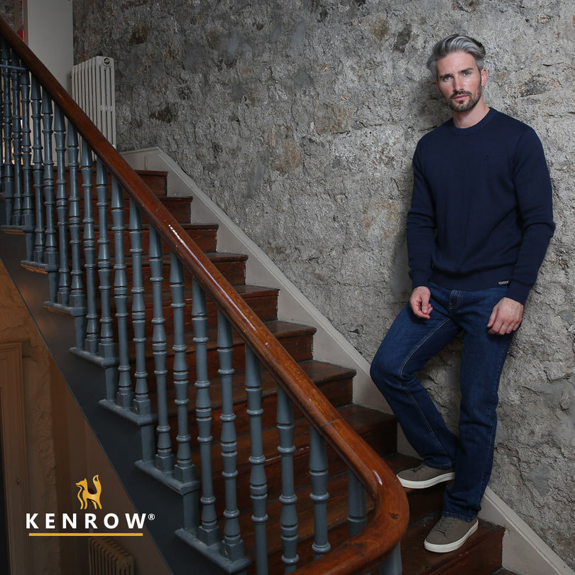 Man wearing a navy melange colour crew neck jumper standing on a stairs