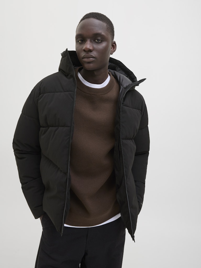 Person wearing a black puffer jacket over a brown sweater on a plain background