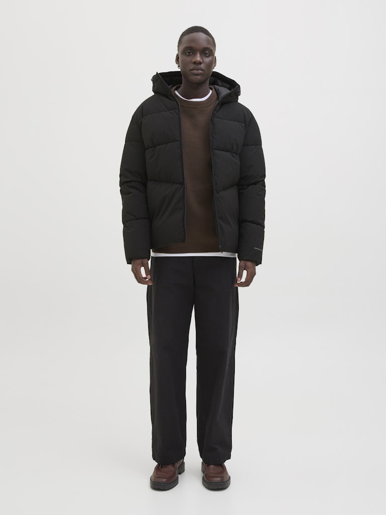Person wearing a black puffer jacket and pants on a white background