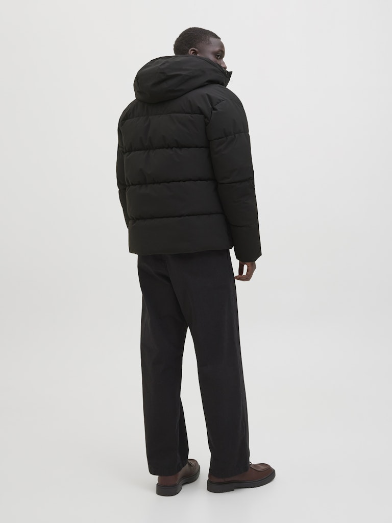 Person wearing a black puffer jacket and pants on a white background